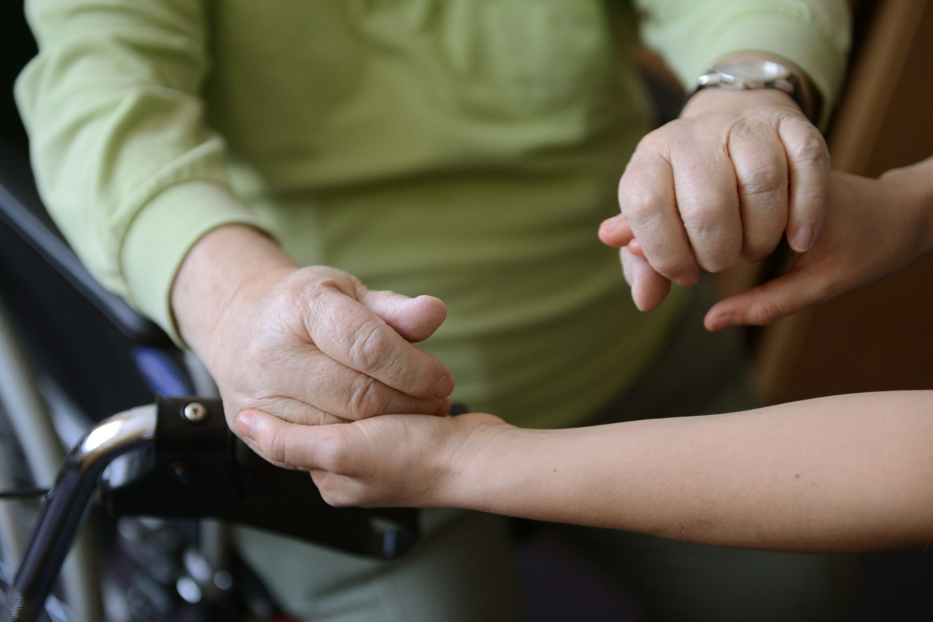 Eine junge Frau hält die Hände eines alten Mannes.