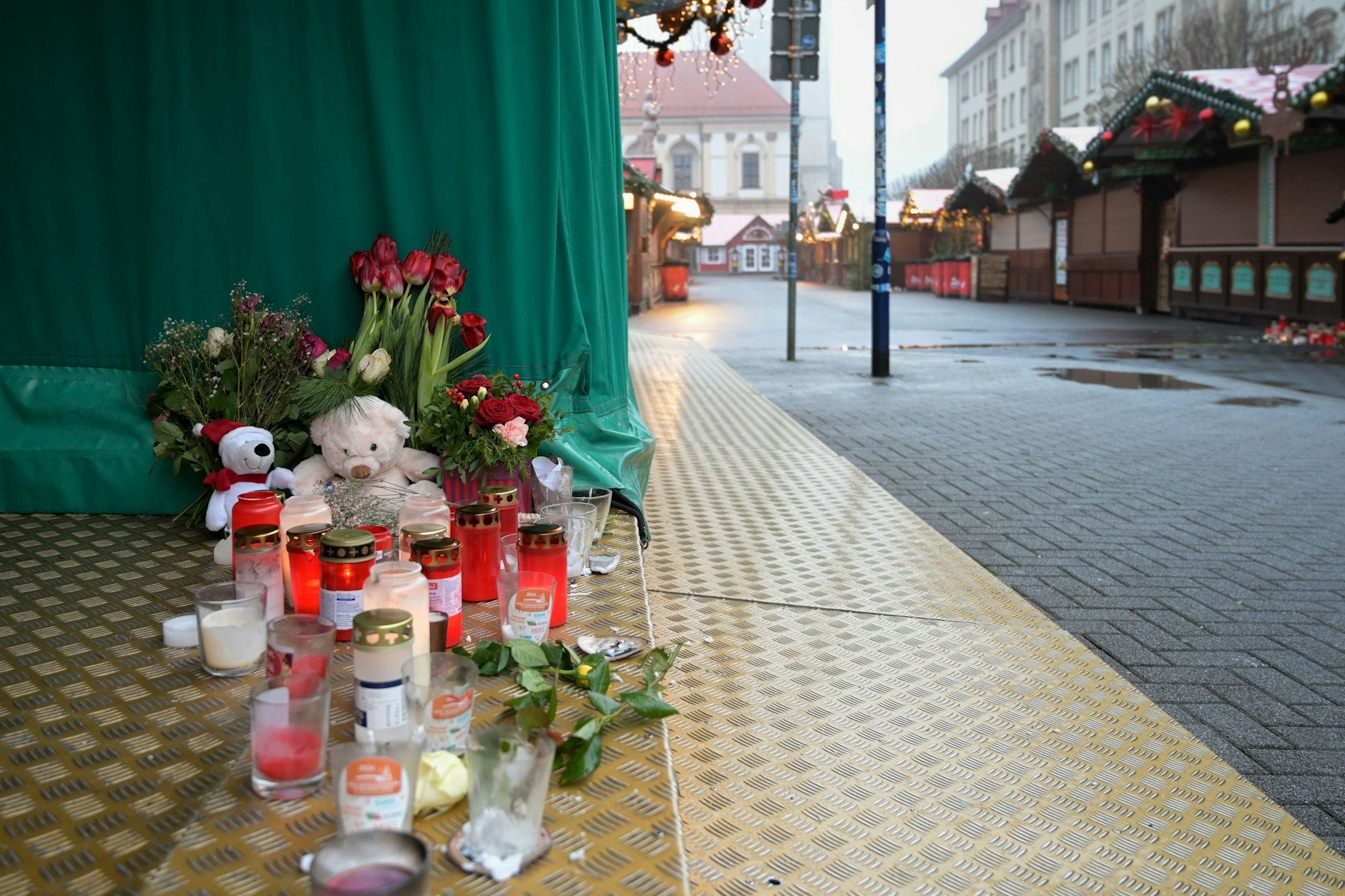 Magdeburg: Kerzen,&nbsp;Kuscheltiere und Blumen stehen auf dem Boden an einem Stand auf dem Weihnachtsmarkt.