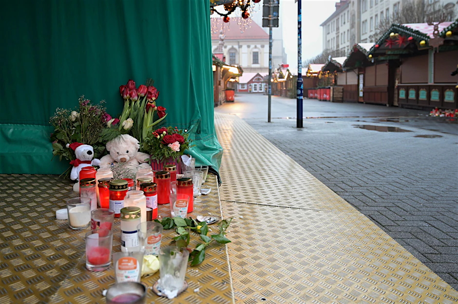 Magdeburg: Kerzen,&nbsp;Kuscheltiere und Blumen stehen auf dem Boden an einem Stand auf dem Weihnachtsmarkt.