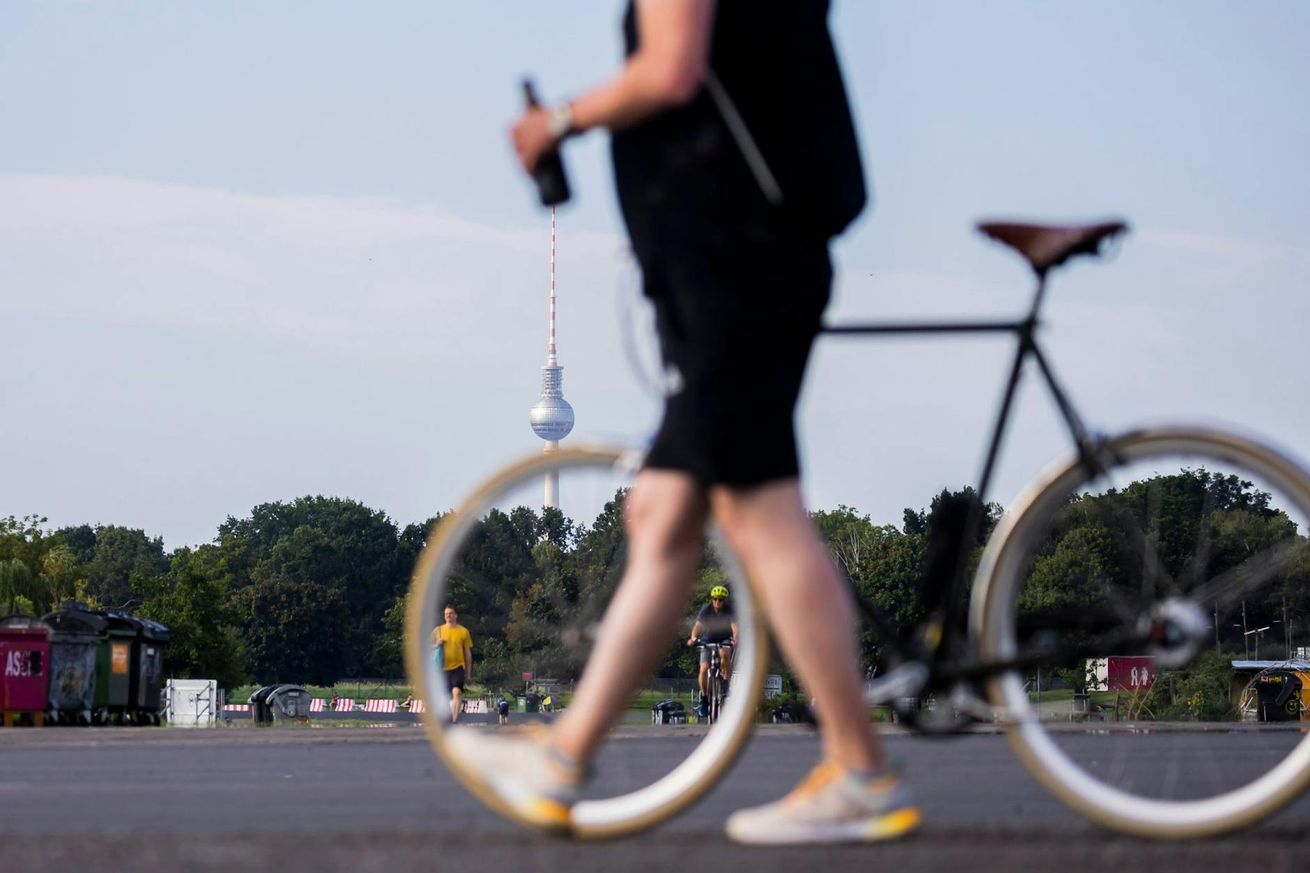 Dit is Berlin: Ein Mann mit Bierflasche in der Hand schiebt ein Fahrrad über das Tempelhofer Feld.