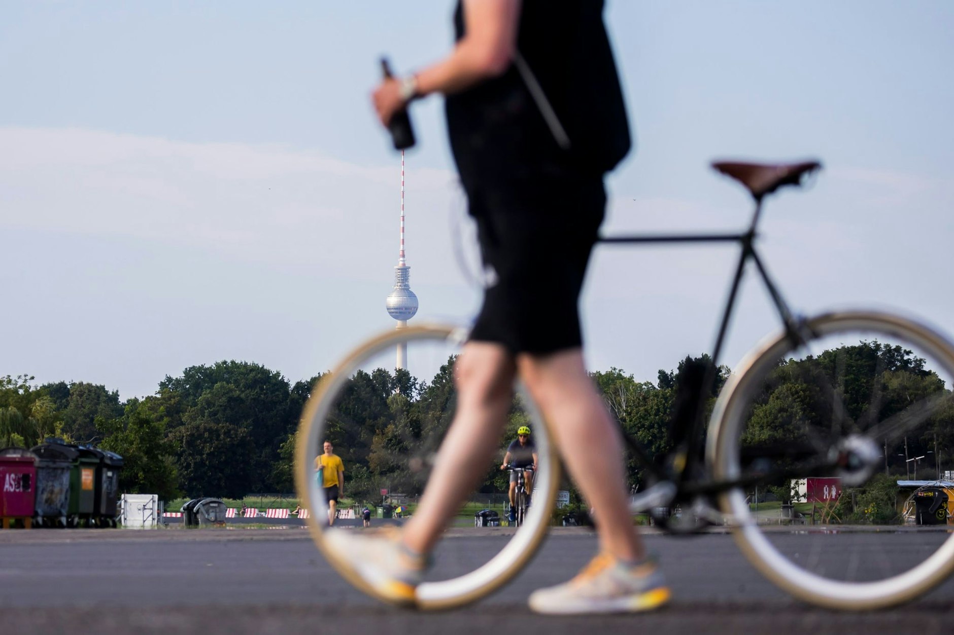 Dit is Berlin: Ein Mann mit Bierflasche in der Hand schiebt ein Fahrrad über das Tempelhofer Feld.