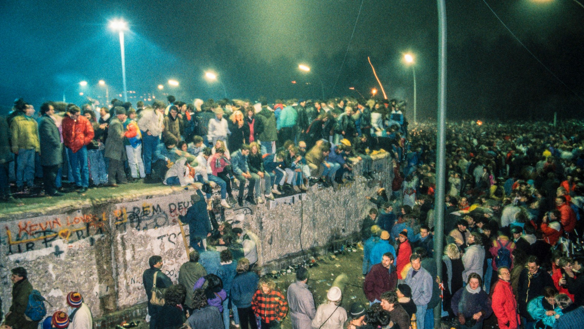 Silvester 1989: Dicht gedrängt stehen die Menschen aus Ost und West auf der Mauer seitlich vom Brandenburger Tor.