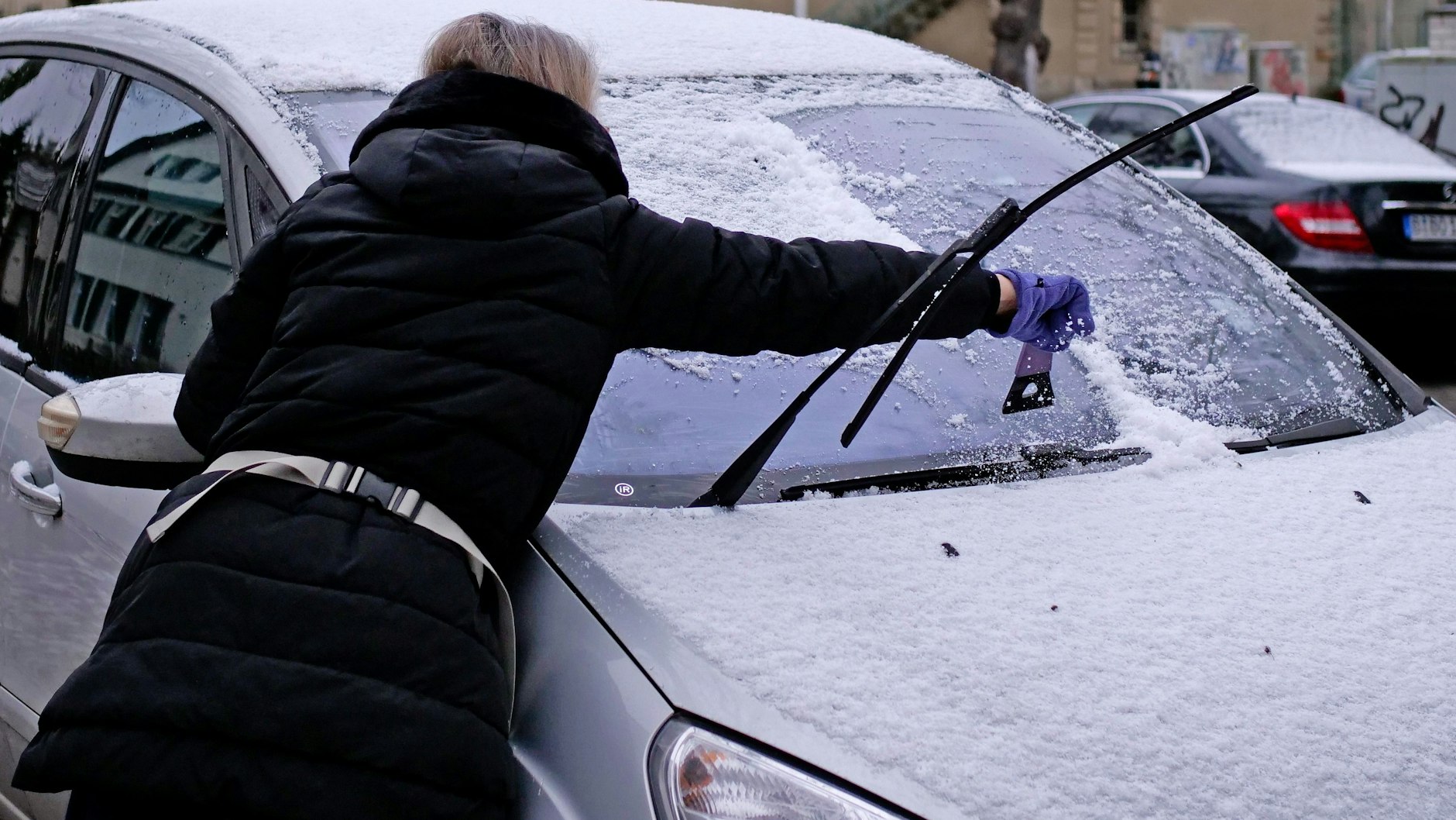 Der Winter hat Berlin erreicht: Eine Frau entfernt im Bezirk Steglitz-Zehlendorf mit einem Eiskratzer Schnee und Eis von der Frontscheibe ihres Autos. 