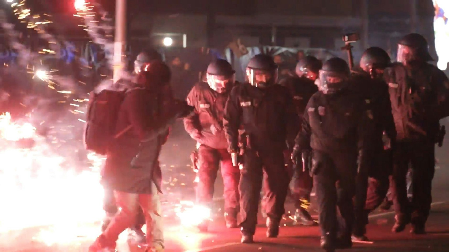 Einsatzkräfte der Polizei stehen in der Silvesternacht zwischen brennendem Feuerwerk in Neukölln.