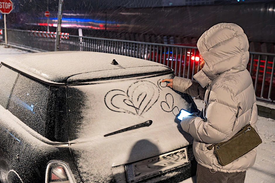 Auf ein schneebedecktes Auto wird ein Herz in die weiße Pracht gemalt.