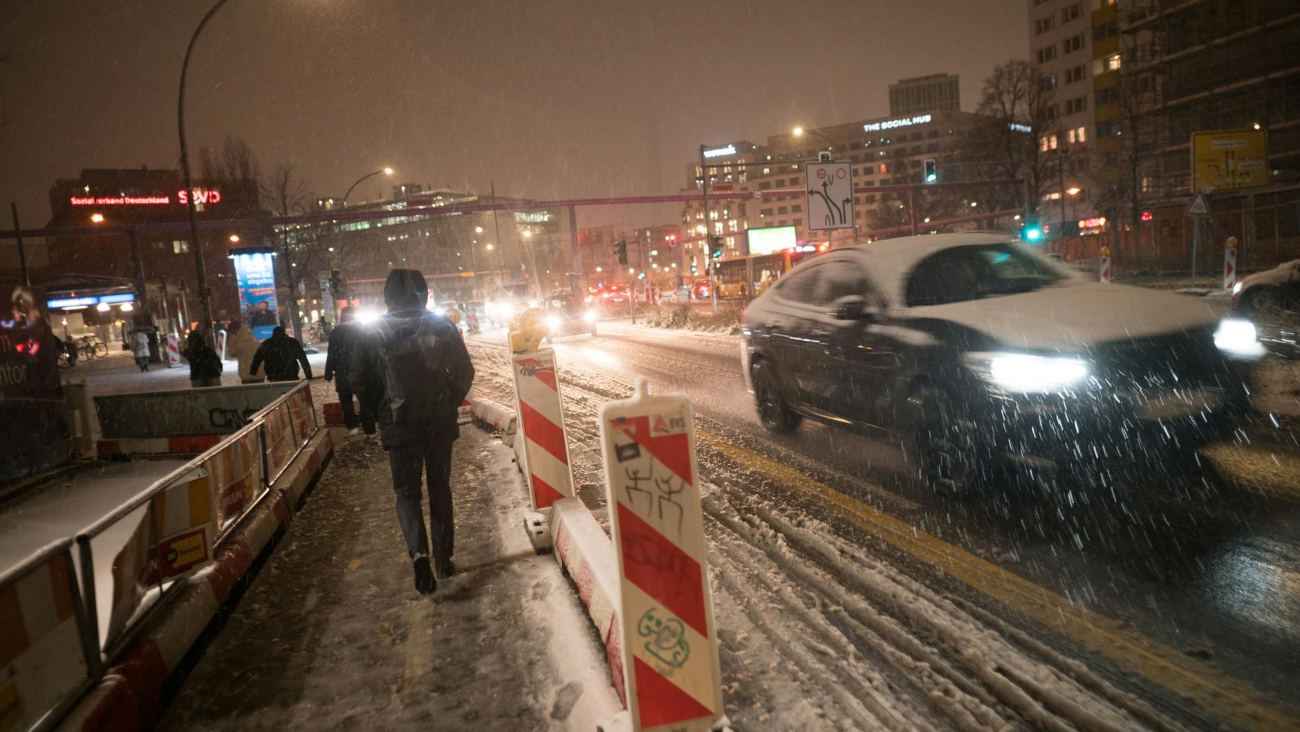 Fußgänger und Autos sind im Berliner Schneegestöber unterwegs.