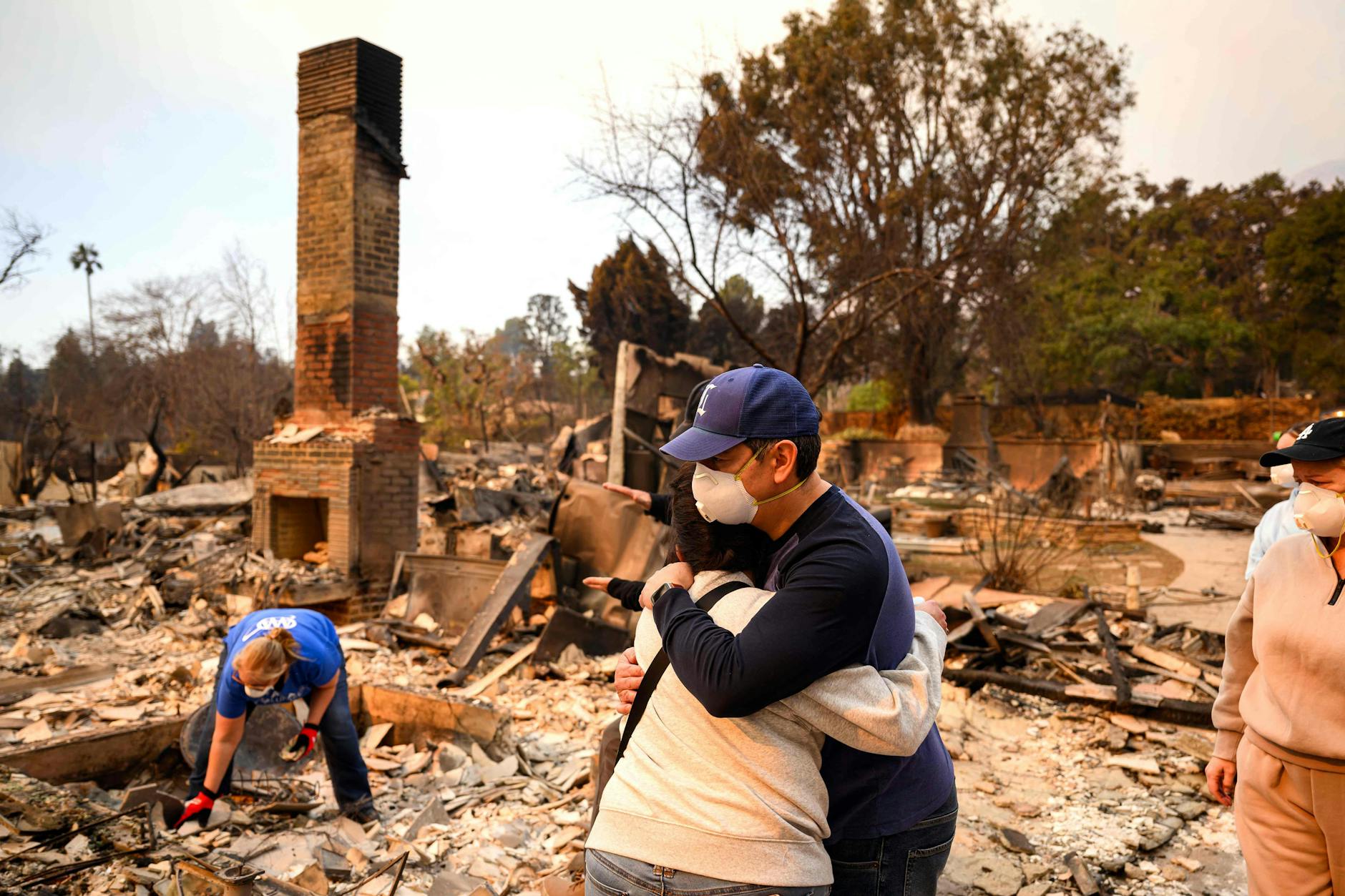 Familienmitglieder stehen vor den Ruinen ihrer verbrannten Häuser und liegen sich in den Armen.