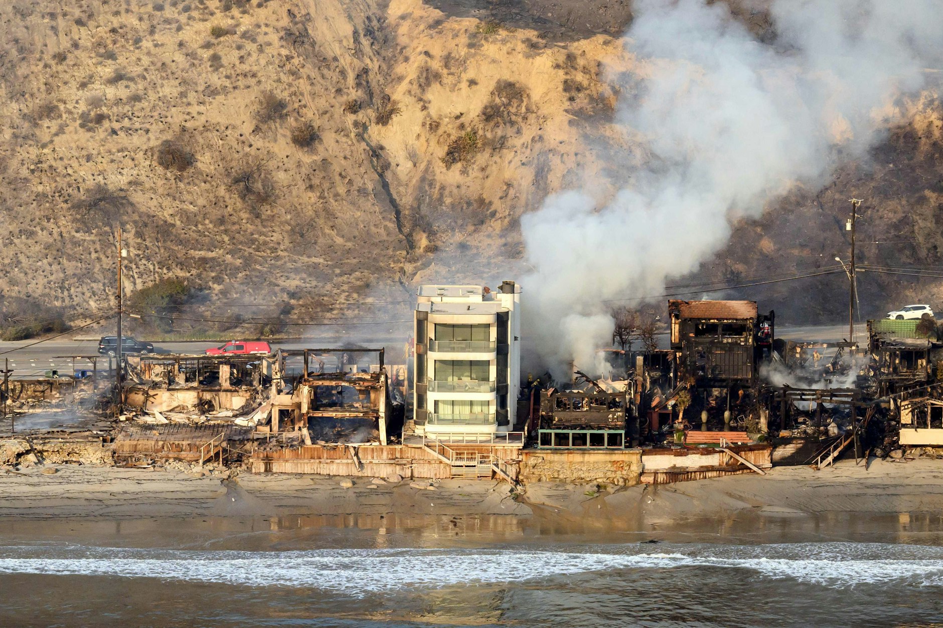 Die Häuserreihe am Strand von Malibu ist bis auf ein Gebäude dem Erdboden gleich, Rauch steigt aus den Trümmern auf.