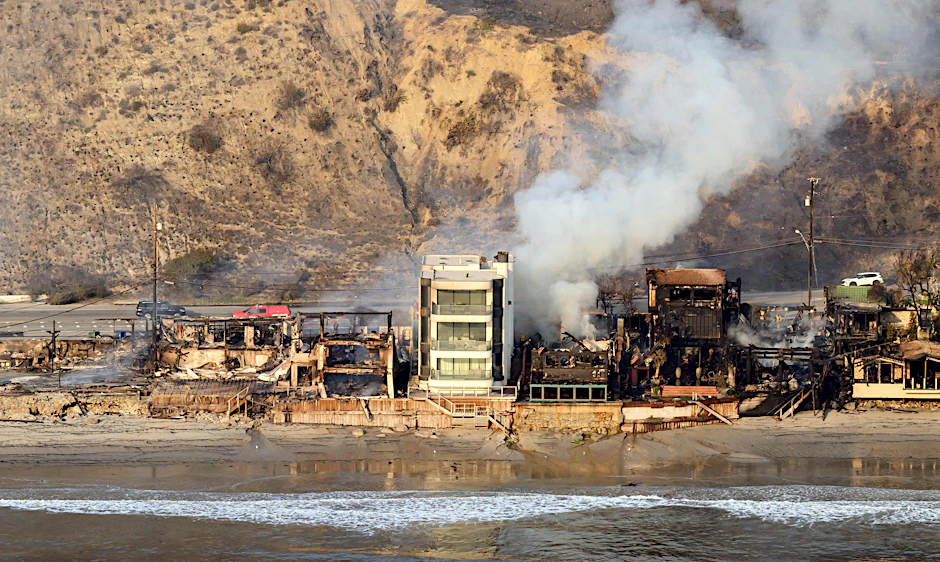 Die Häuserreihe am Strand von Malibu ist bis auf ein Gebäude dem Erdboden gleich, Rauch steigt aus den Trümmern auf.