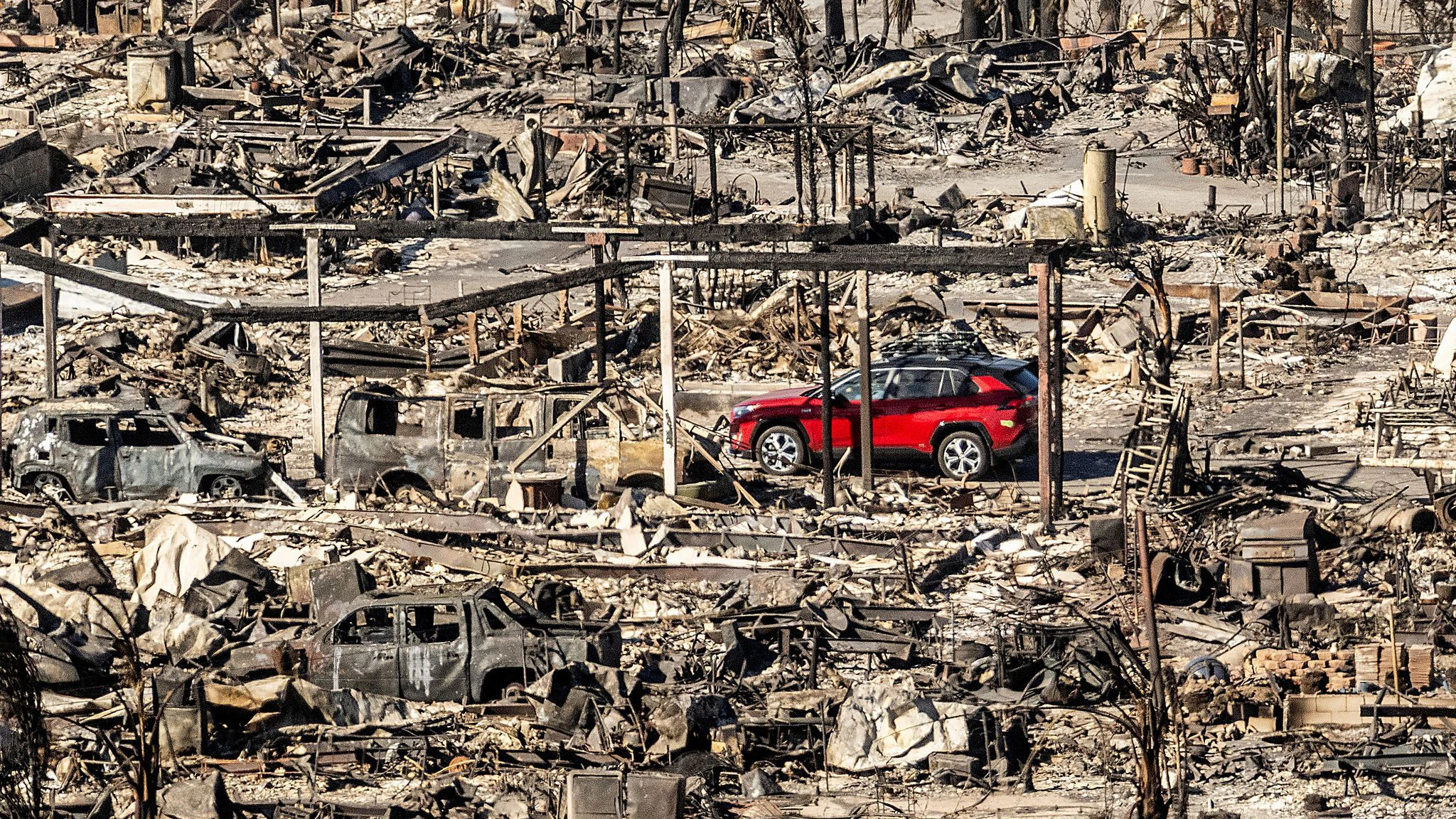 Ein rotes Auto fährt an Häusern und Fahrzeugen vorbei, die durch das Palisades-Feuer in den Pacific Palisades Bowl Mobile Estates zerstört wurden.