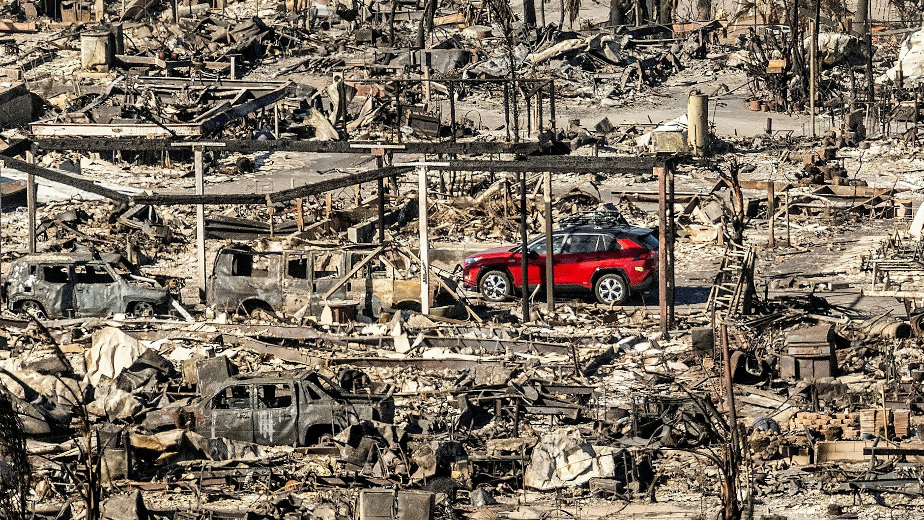 Ein rotes Auto fährt an Häusern und Fahrzeugen vorbei, die durch das Palisades-Feuer in den Pacific Palisades Bowl Mobile Estates zerstört wurden.
