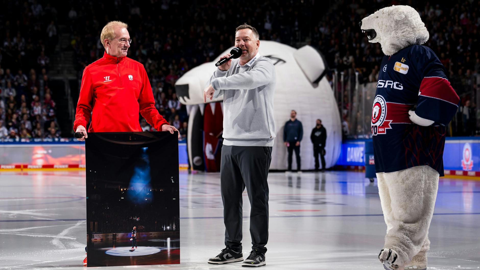 Klar, dass da der Boss persönlich gratuliert: Eisbären-Geschäftsführer Thomas Bothstede (M.) bedankt sich bei Uwe Schumann für 1000 Spiele am Hallen-Mikro, da ist auch Maskottchen Bully von den Socken.