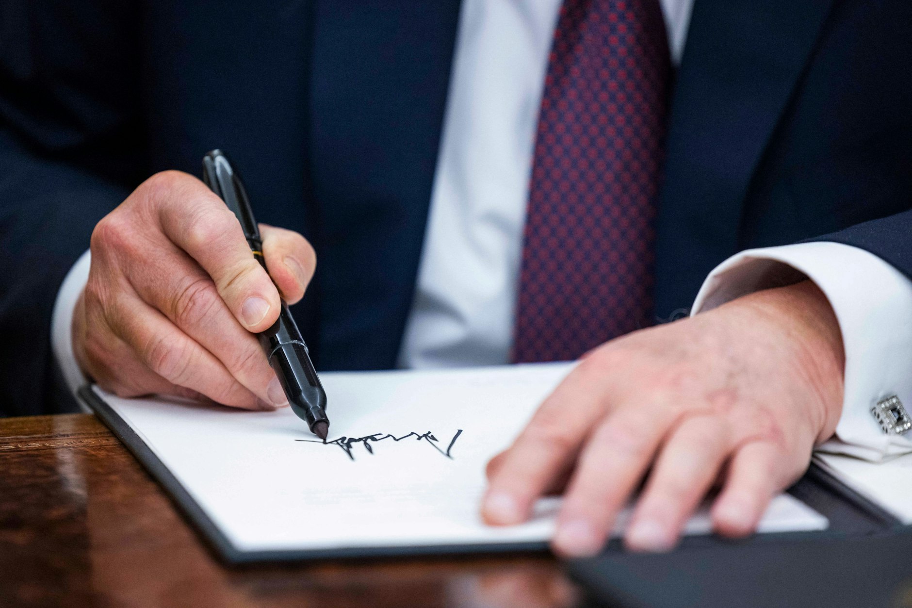 Donald Trump setzt seine Unterschrift unter ein Dokument.