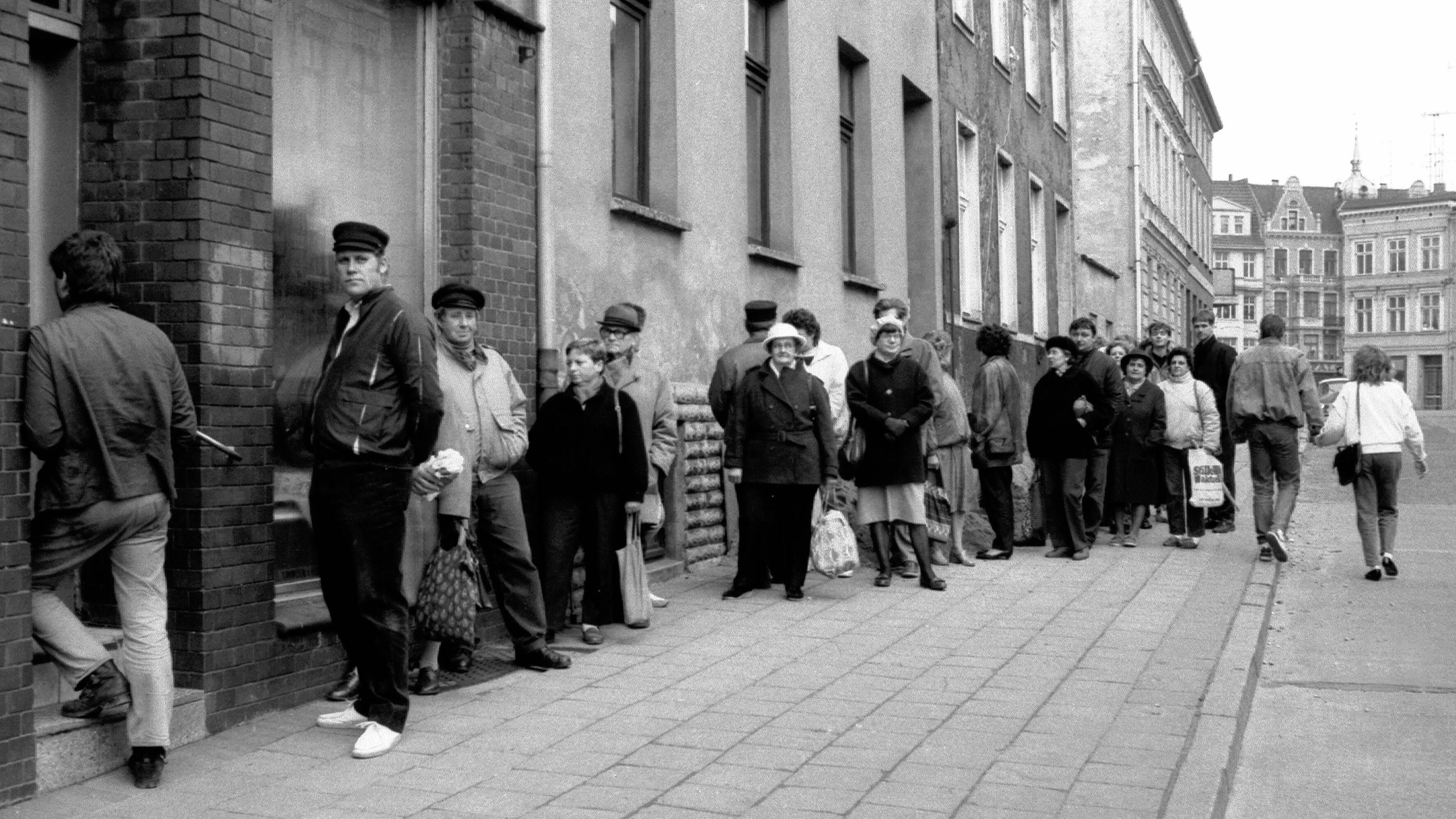Menschen warten in einer Schlange vor einer Bäckerei in Rostock. Auch die Mangelwirtschaft wird in etlichen Witzen aus der DDR aufs Korn genommen.