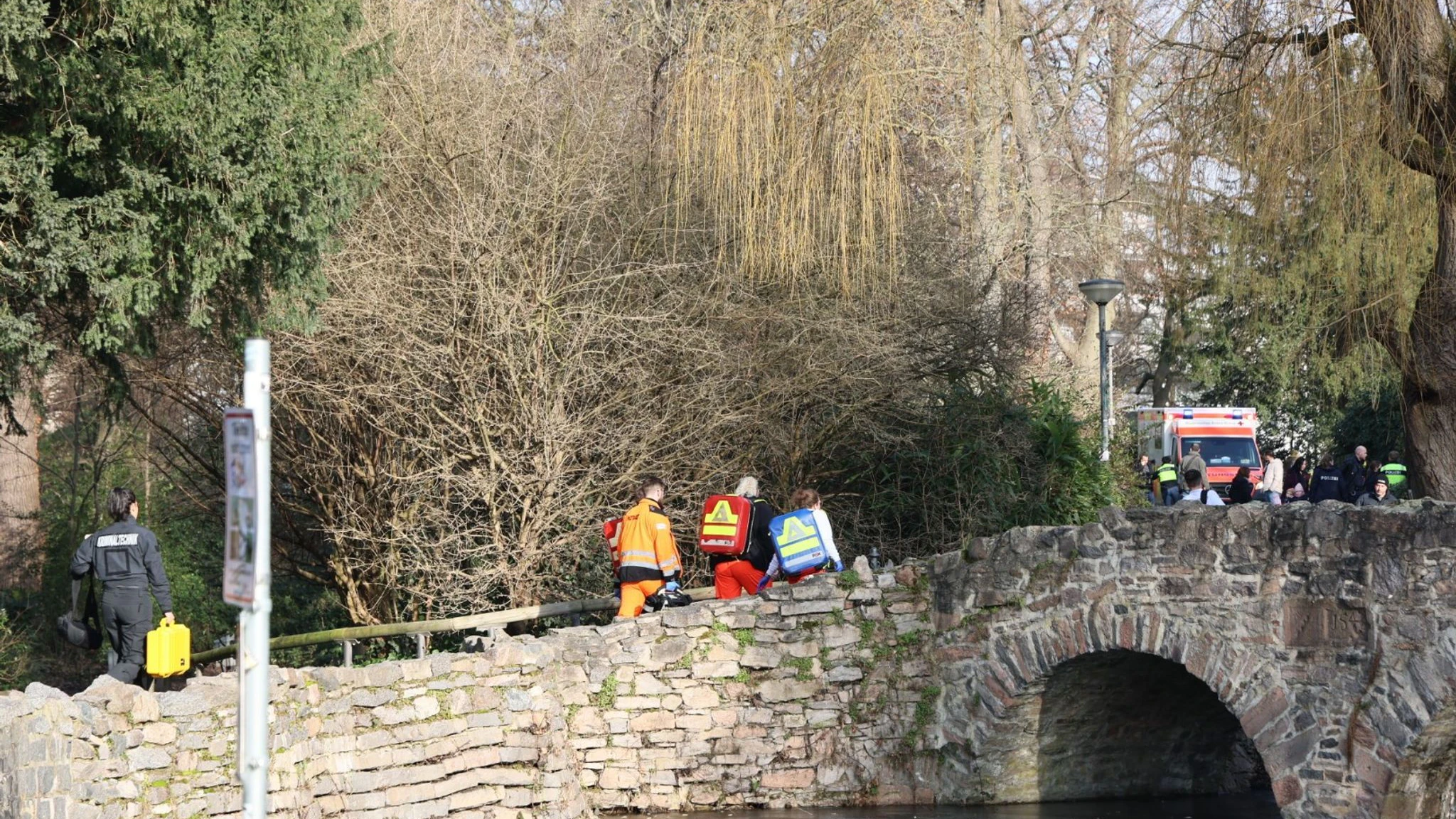 Rettungskräfte und Kriminaltechniker gehen in der Nähe eines Tatortes eine kleine Brücke hinauf. Bei einer Gewalttat in einem Park sind nach ersten Erkenntnissen mehrere Menschen erstochen worden.