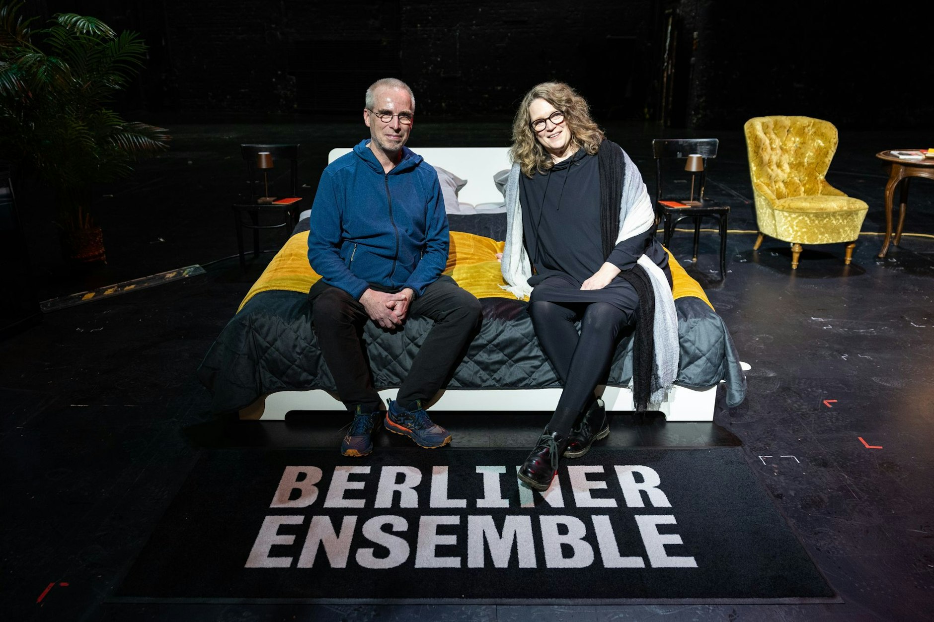 Stefanie und Christoph Siegmann (l.) sitzen auf einem Bett auf der Bühne im Berliner Ensemble.