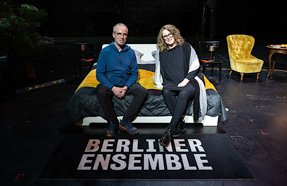 Stefanie und Christoph Siegmann (l.) sitzen auf einem Bett auf der Bühne im Berliner Ensemble. 