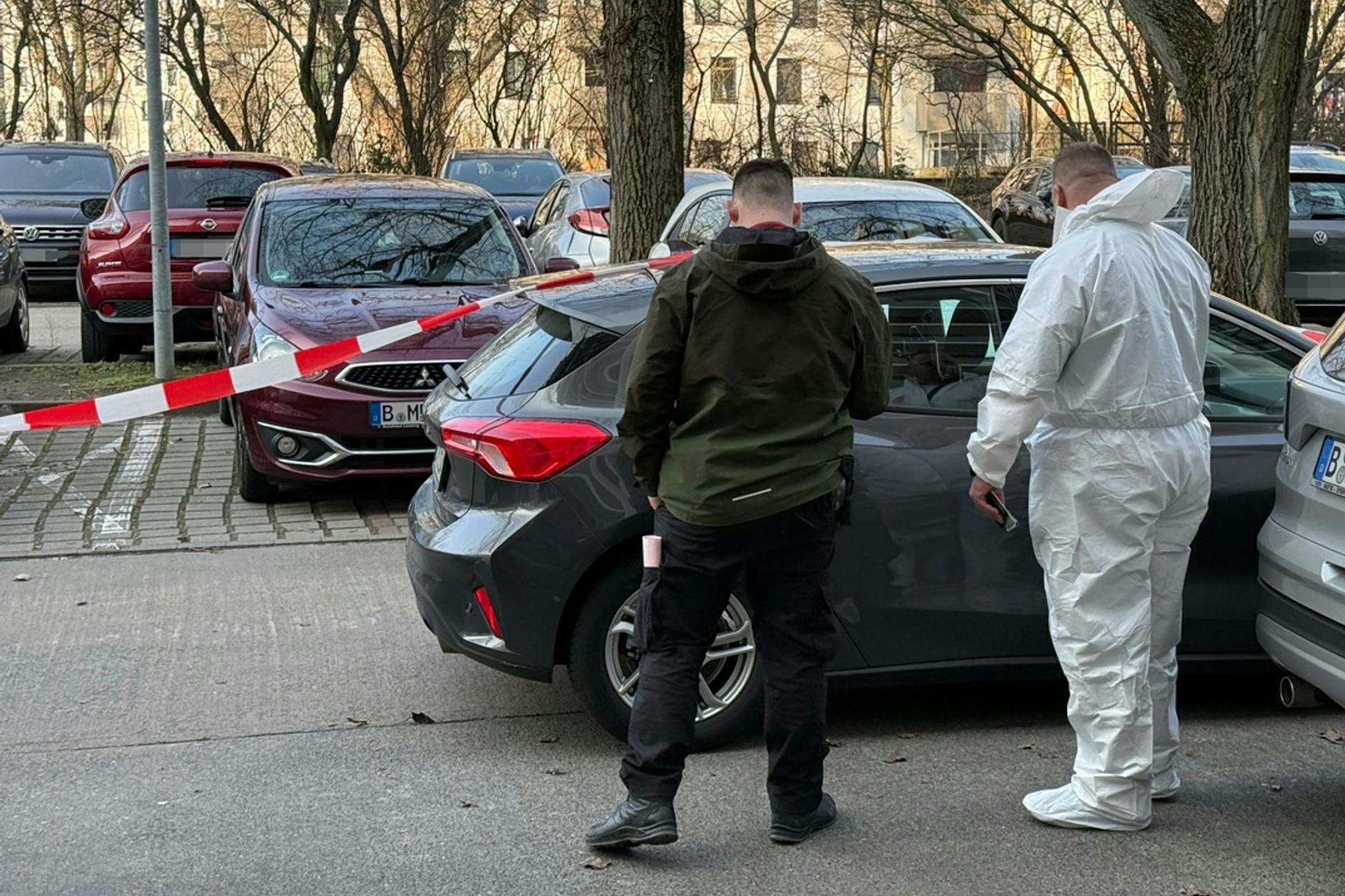 Zwei Beamte der Spurensicherung stehen vor einem Auto, das mit Absperrband gesichert ist.