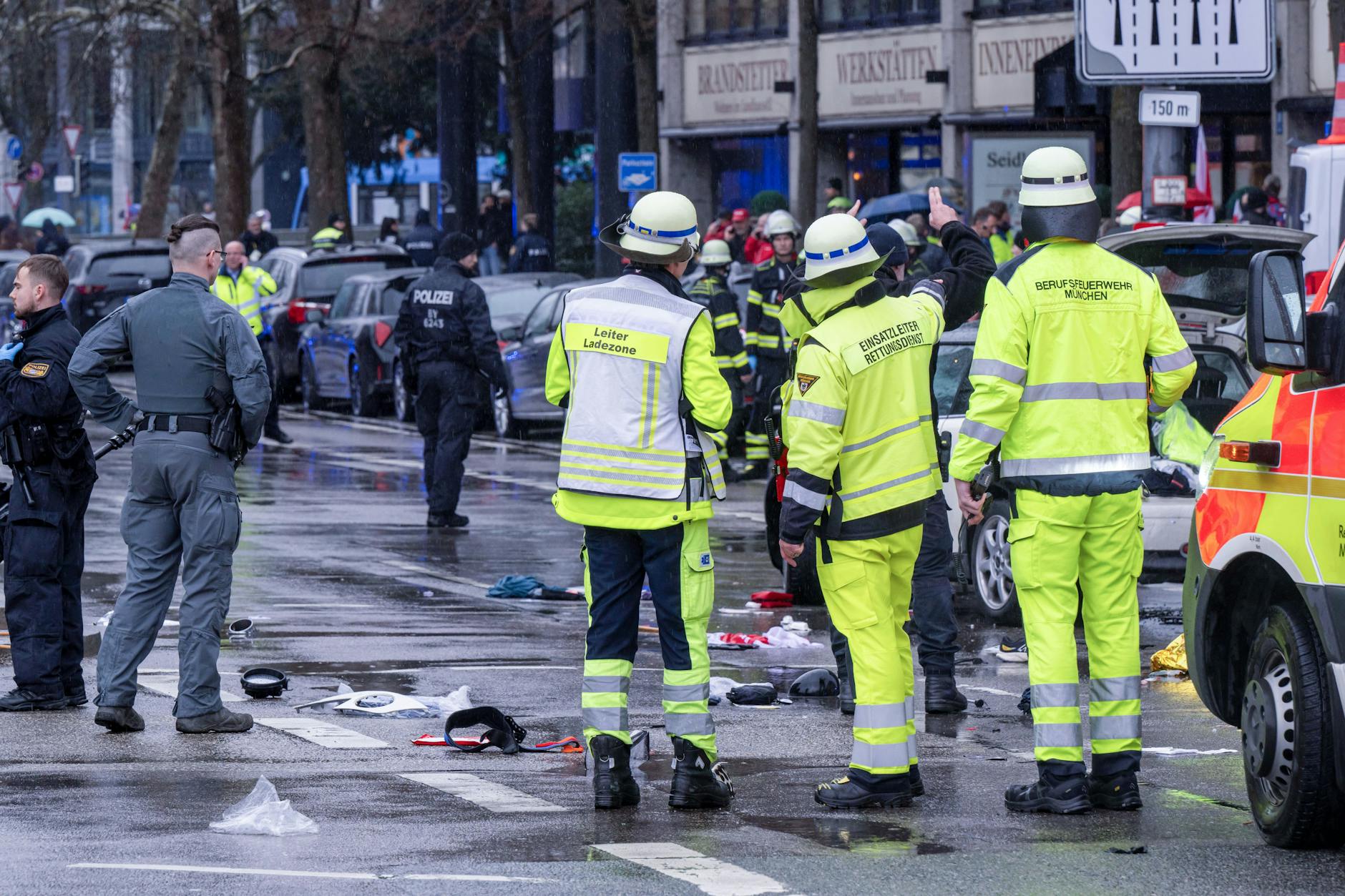 Feuerwehrleute und Polizisten stehen am Einsatzort. In der Münchner Innenstadt ist ein Fahrzeug in eine Menschengruppe gefahren.