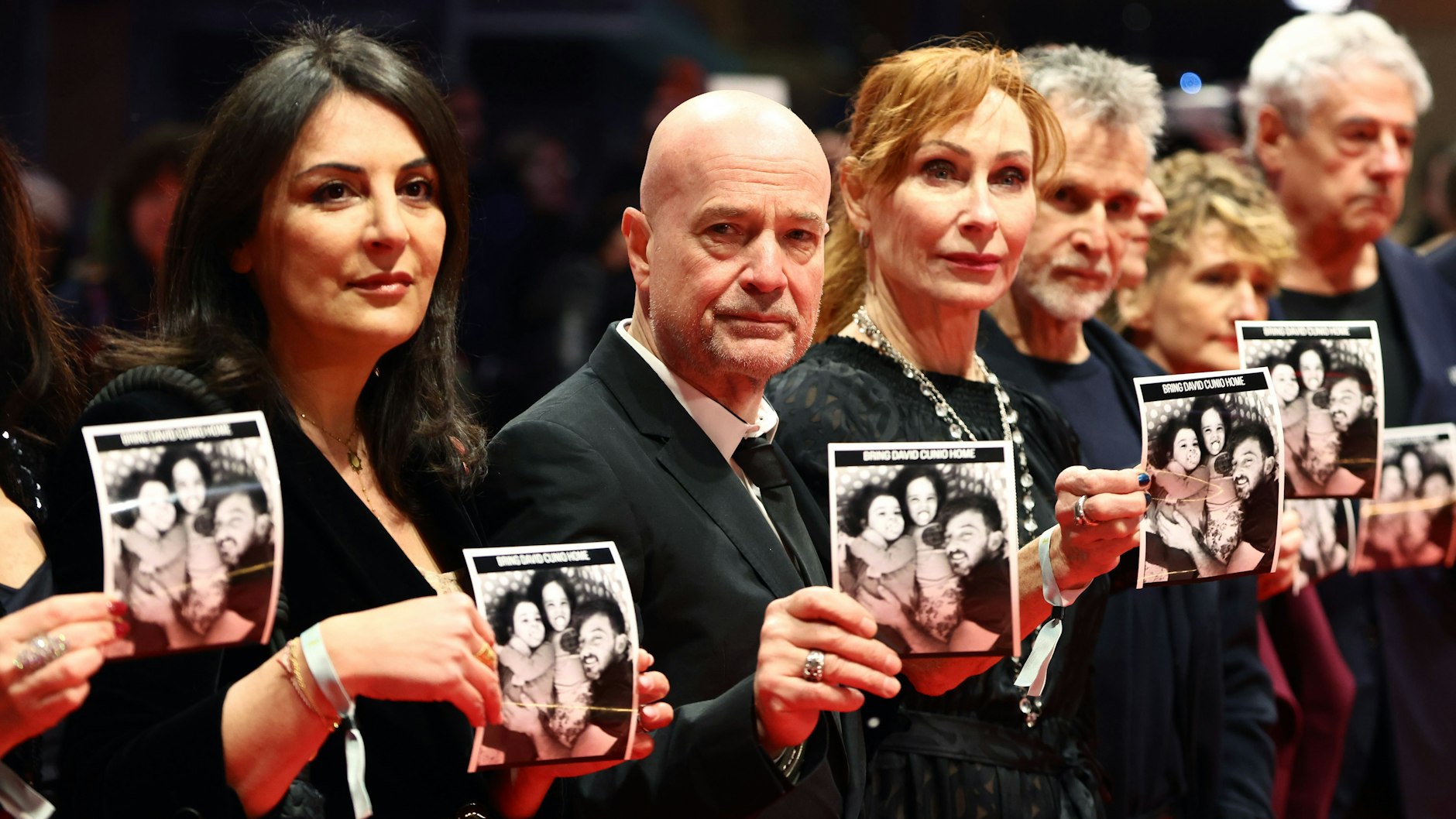 Menschenrechtsaktivistin Düzen Tekkal (v.l.), Schauspieler Christian Berkel, Schauspielerin Andrea Sawatzki, Schauspieler Ulrich Matthes und Berlinale-Chefin Tricia Tuttle stehen am Eröffnungsabend der Berlinale auf dem Roten Teppich und zeigen Fotos der israelischen Geisel David Cunio.