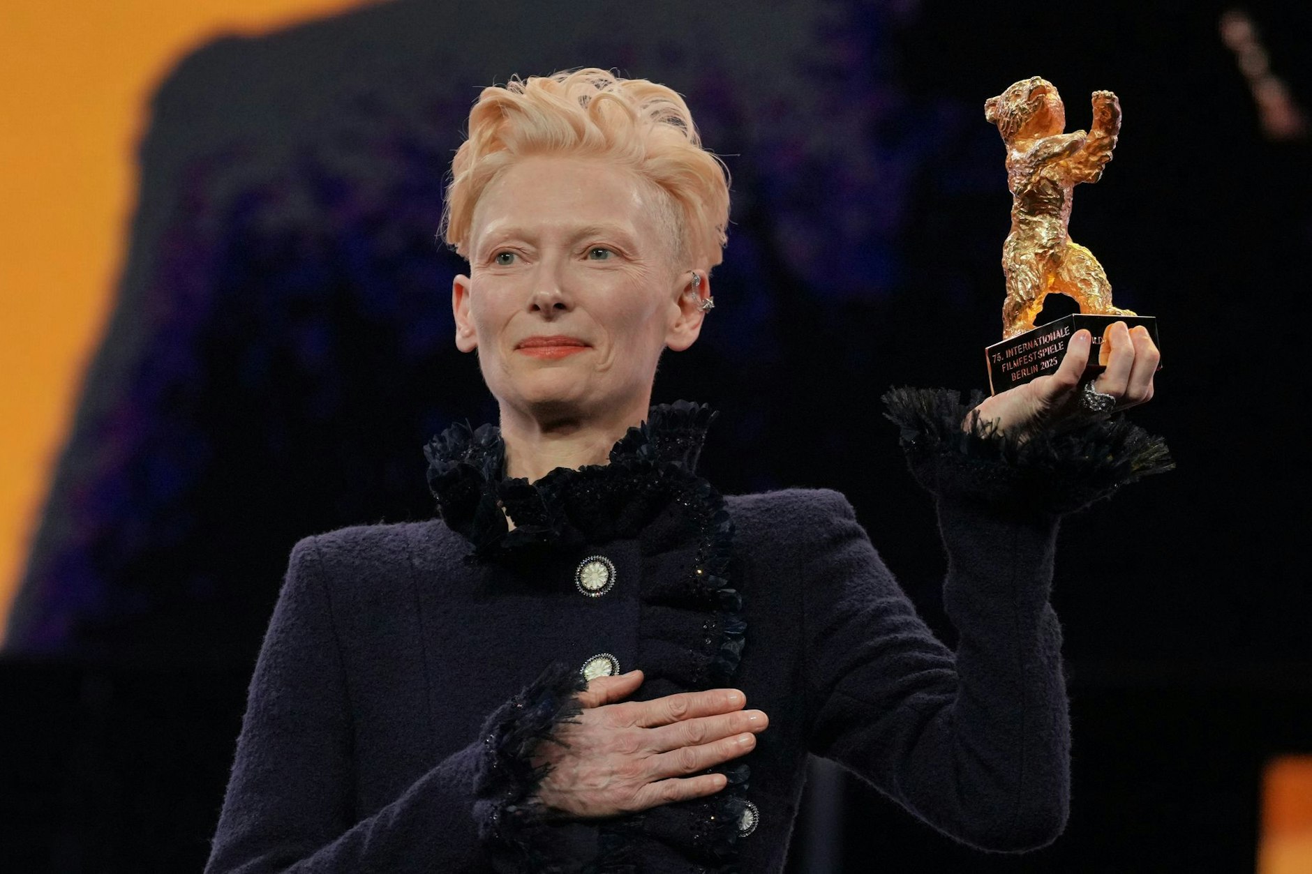 Tilda Swinton steht während der Eröffnung der Berlinale auf der Bühne und hält ihren goldenen Ehrenbär hoch.