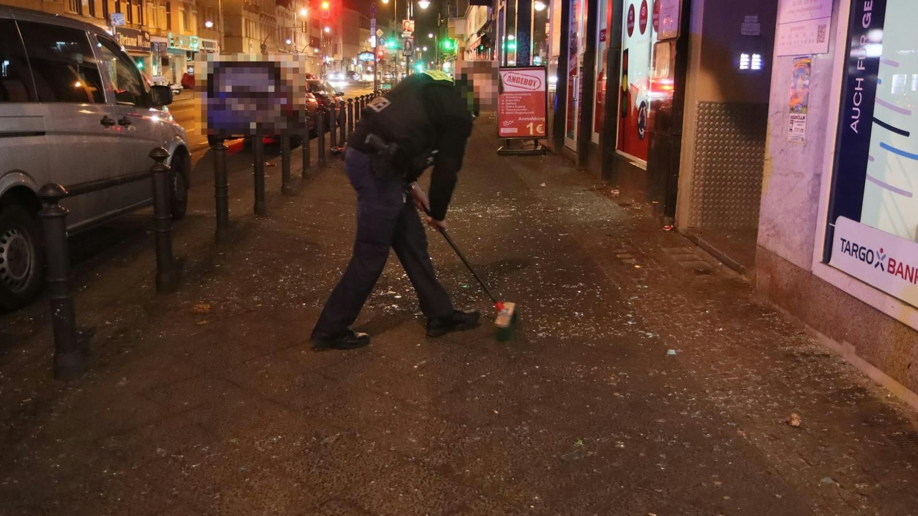 Ein Beamter der Polizei beseitigt die Glassplitter: Nach einer Explosion in Neukölln lagen auf dem Bürgersteig in der Karl-Marx-Straße überall Scherben.
