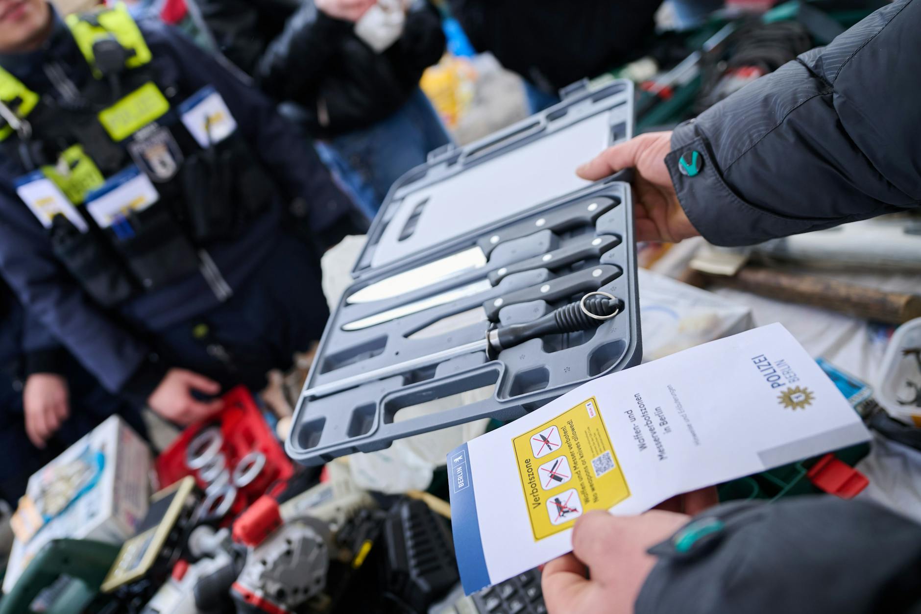 Ein Marktstandbesitzer fragt die Polizei, ob er weiterhin Küchenmesser verkaufen darf, während die Beamten Flyer in unterschiedlichen Sprachen auf dem Leopoldplatz verteilen. Seit dem 15. Februar gibt es Messerverbotszonen im Görlitzer Park, am Kottbusser Tor und am Leopoldplatz.