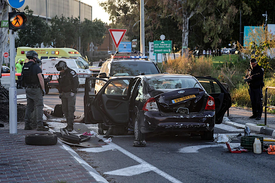 Israelische Polizisten untersuchen das Tatfahrzeug, daneben liegt der erschossene Fahrer.