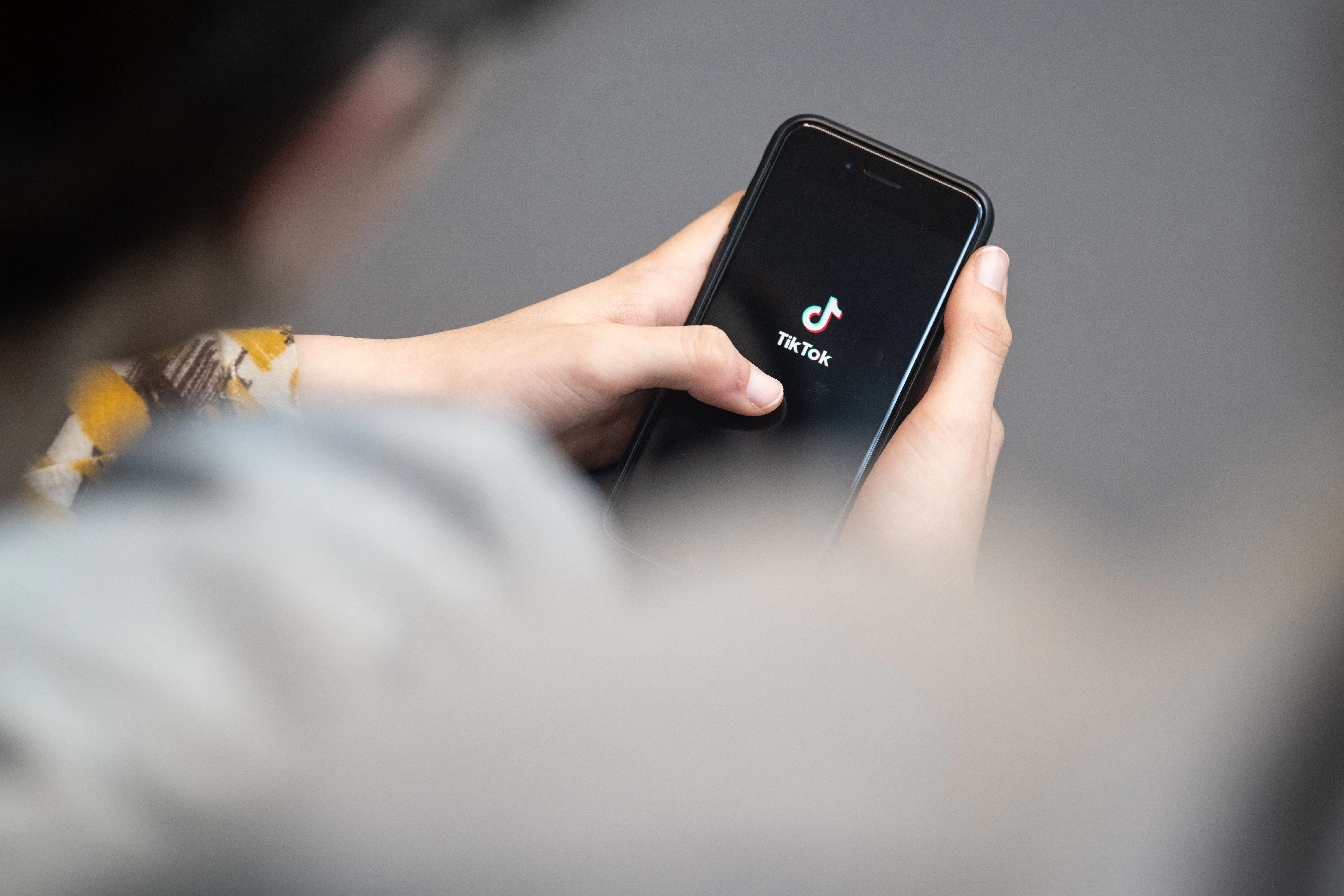 Eine Jugendliche schaut auf ein Smartphone mit angezeigtem TikTok-Logo.