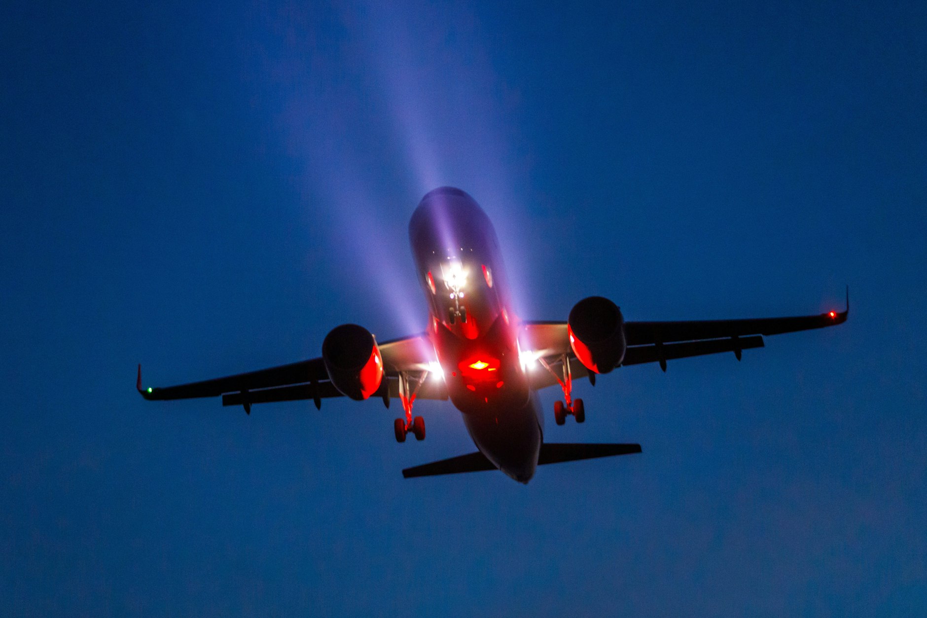 Ein Passagierflugzeug ist am Abend mit ausgefahrenem Fahrwerk und Scheinwerferlicht im Landeanflug auf den BER Hauptstadtflughafen.