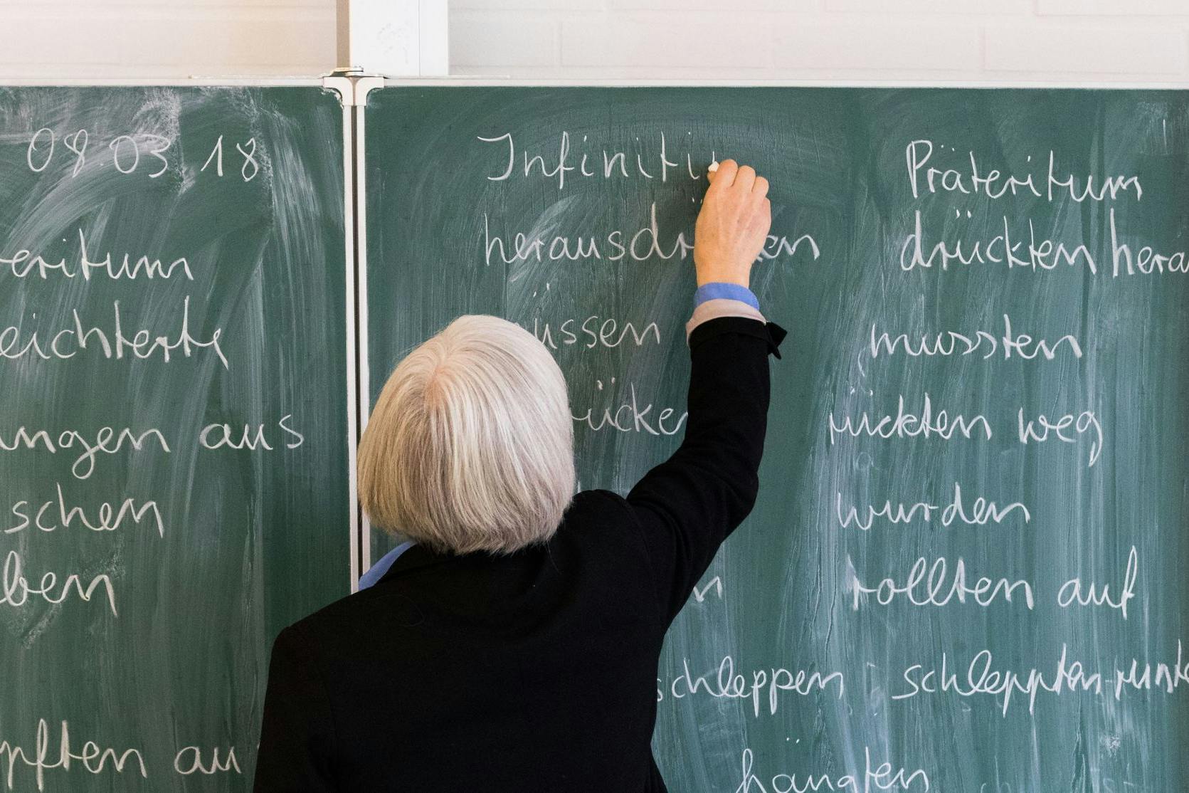 Eine Lehrerin steht in einem Klassenraum an einer Tafel und schreibt. Nur wenige Kinder bestehen den ersten Probeunterricht fürs Gymnasium.