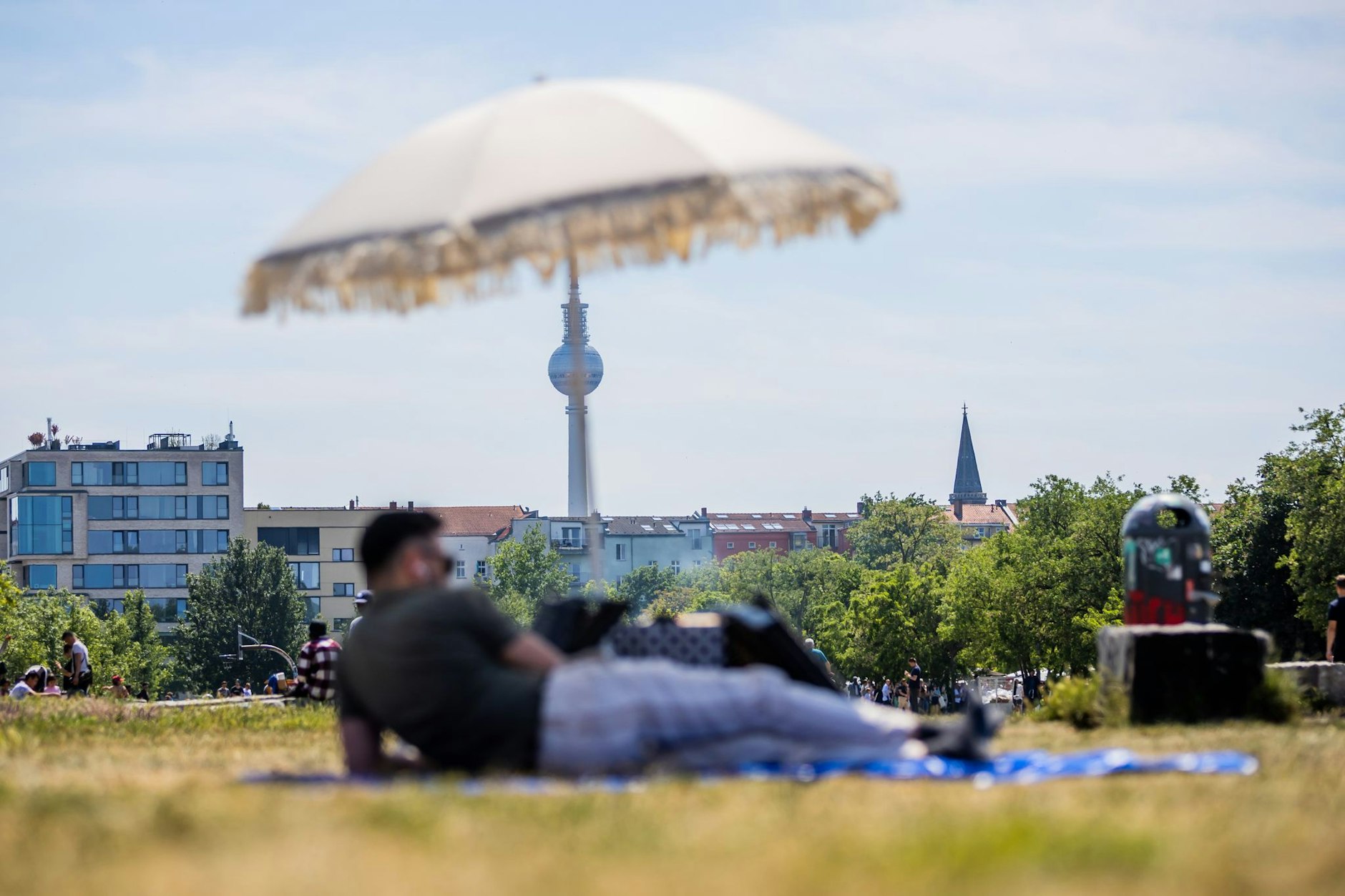 Ein Mann liegt im Mauerpark vor dem Berliner Fernsehturm unter einem Sonnenschirm.