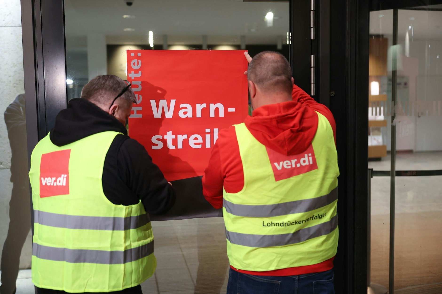 Streikende befestigen ein Plakat mit der Aufschrift „Warnstreik“ am Terminal des Flughafens BER, als es dort im Frühjahr 2023 zu einem Ausstand kam.
