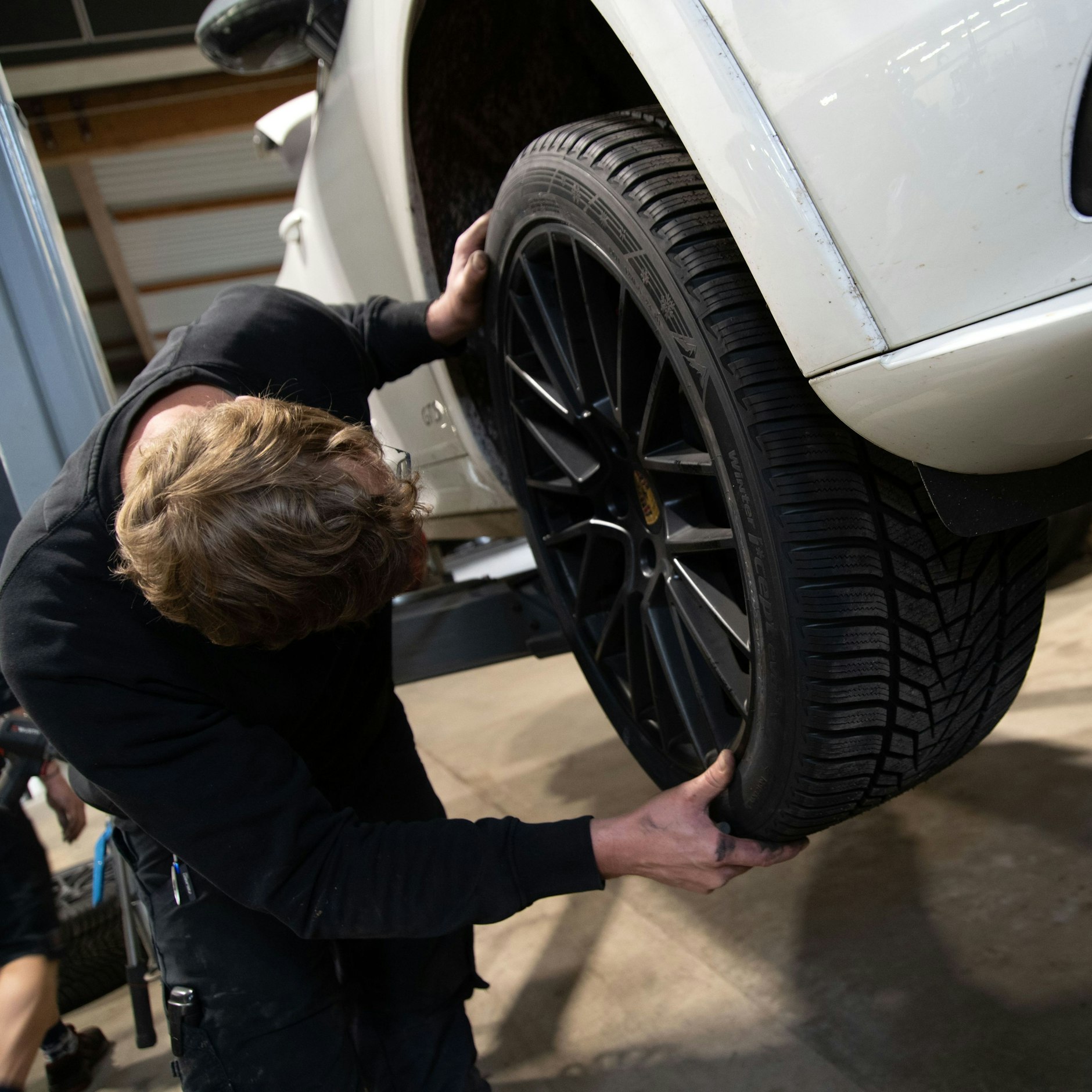 Ein Kfz-Mechaniker montiert ein Rad an einem Pkw. Es ist Zeit für den Reifenwechsel.