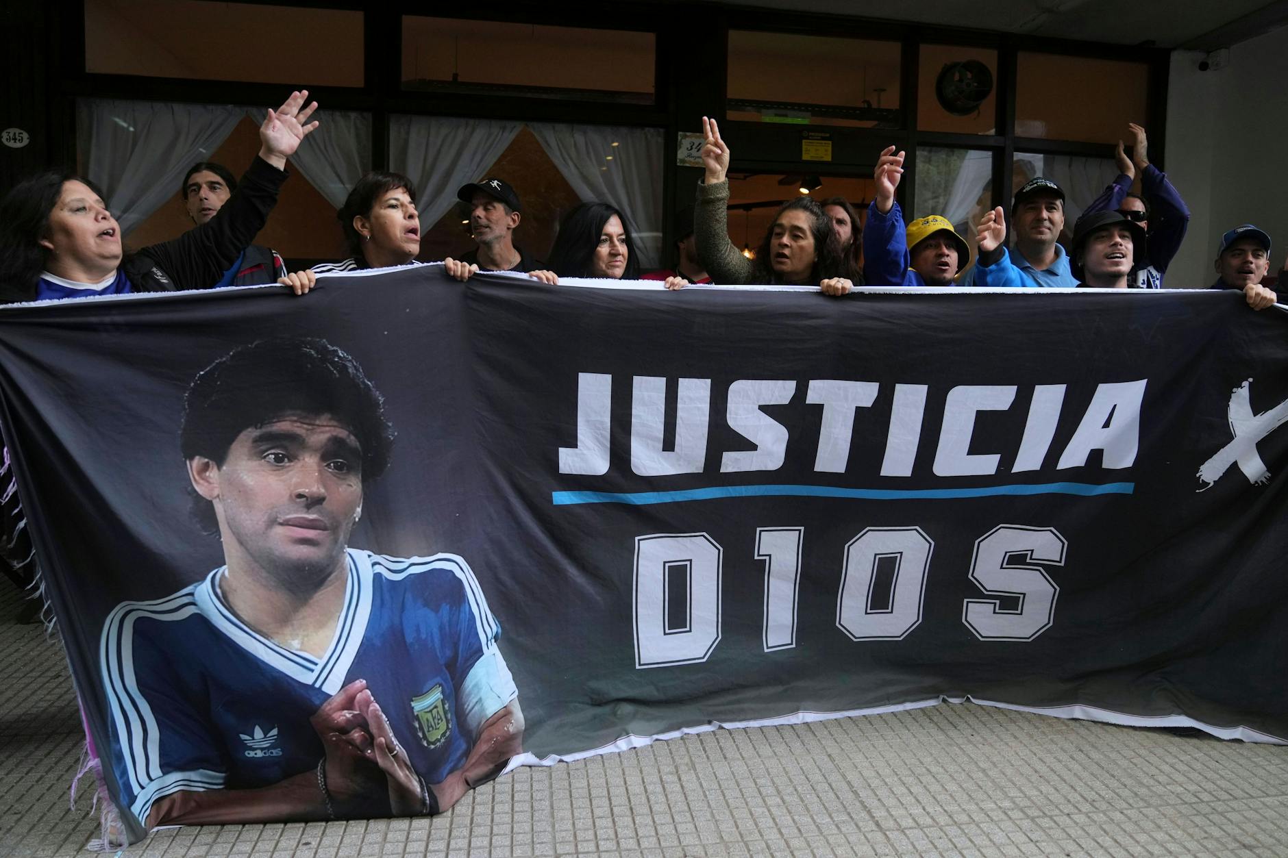 Fans des verstorbenen Fußballstars Diego Maradona halten ein Transparent mit der spanischen Aufschrift „Gerechtigkeit für Gott“ vor dem Gericht hoch.
