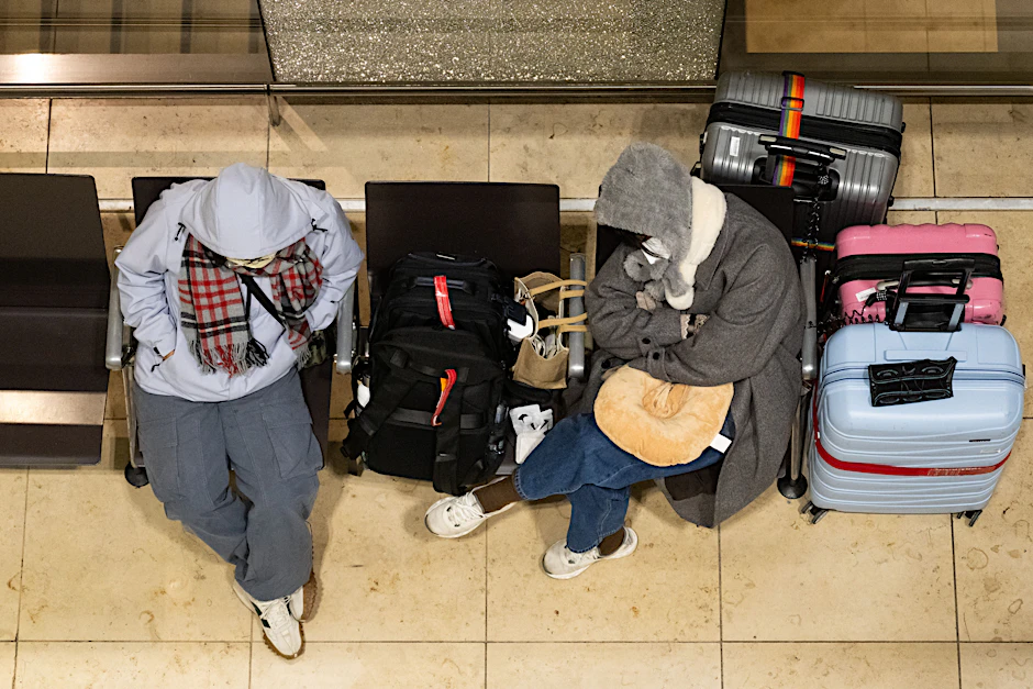 Zwei Reisende sitzen am Flughafen Berlin-Brandenburg BER mit ihrem Gepäck im Terminal.