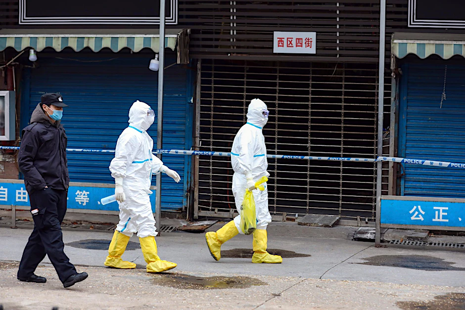 Arbeiter in Schutzkleidung tragen eine Tasche auf dem Huanan Seafood Market.