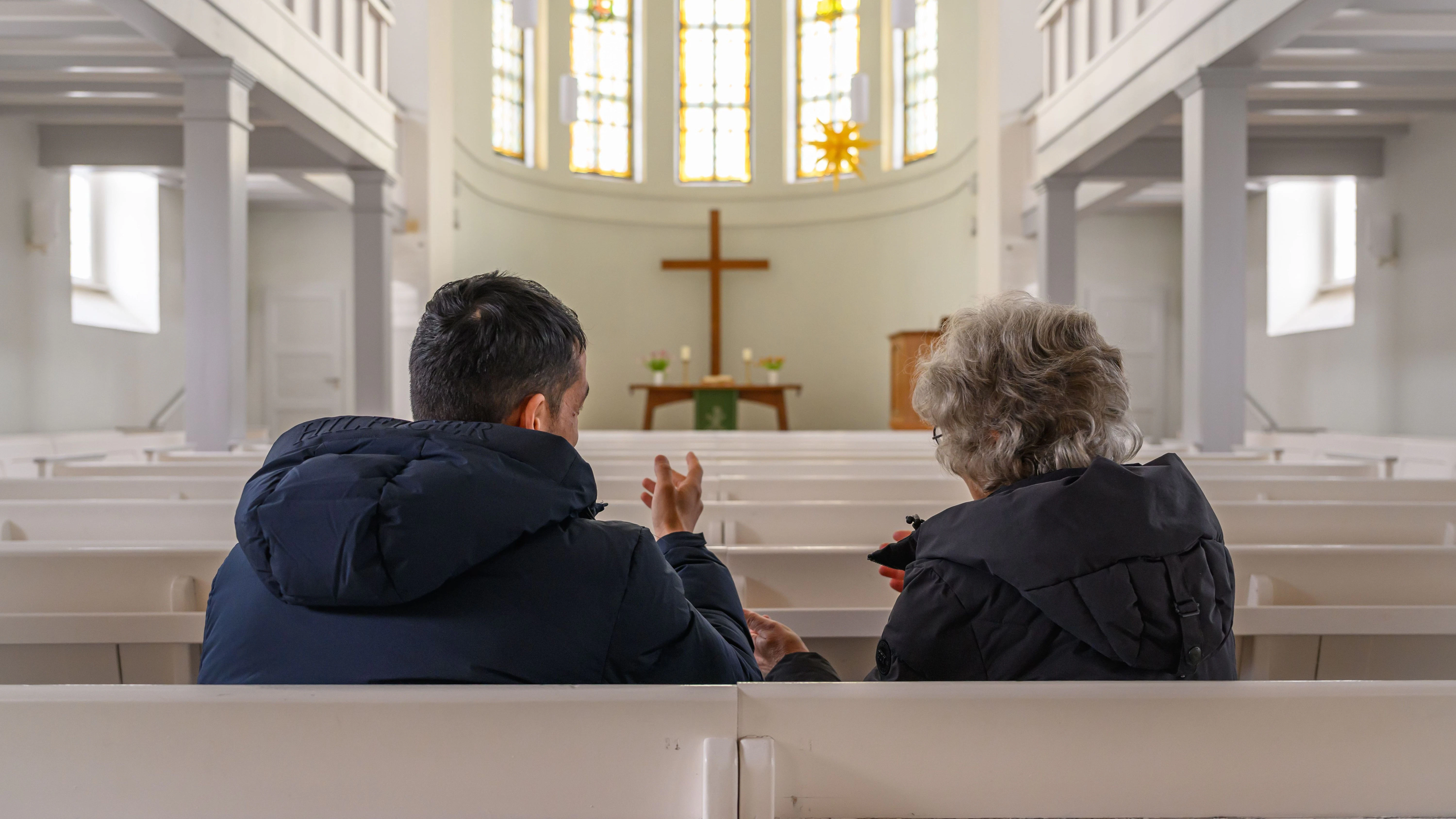 In der Kirche von Seelow unterhält sich eine Frau der Kirchengemeinde mit einem Geflüchteten aus Afghanistan. Die Bezahlkarte für Asylbewerber ist umstritten.