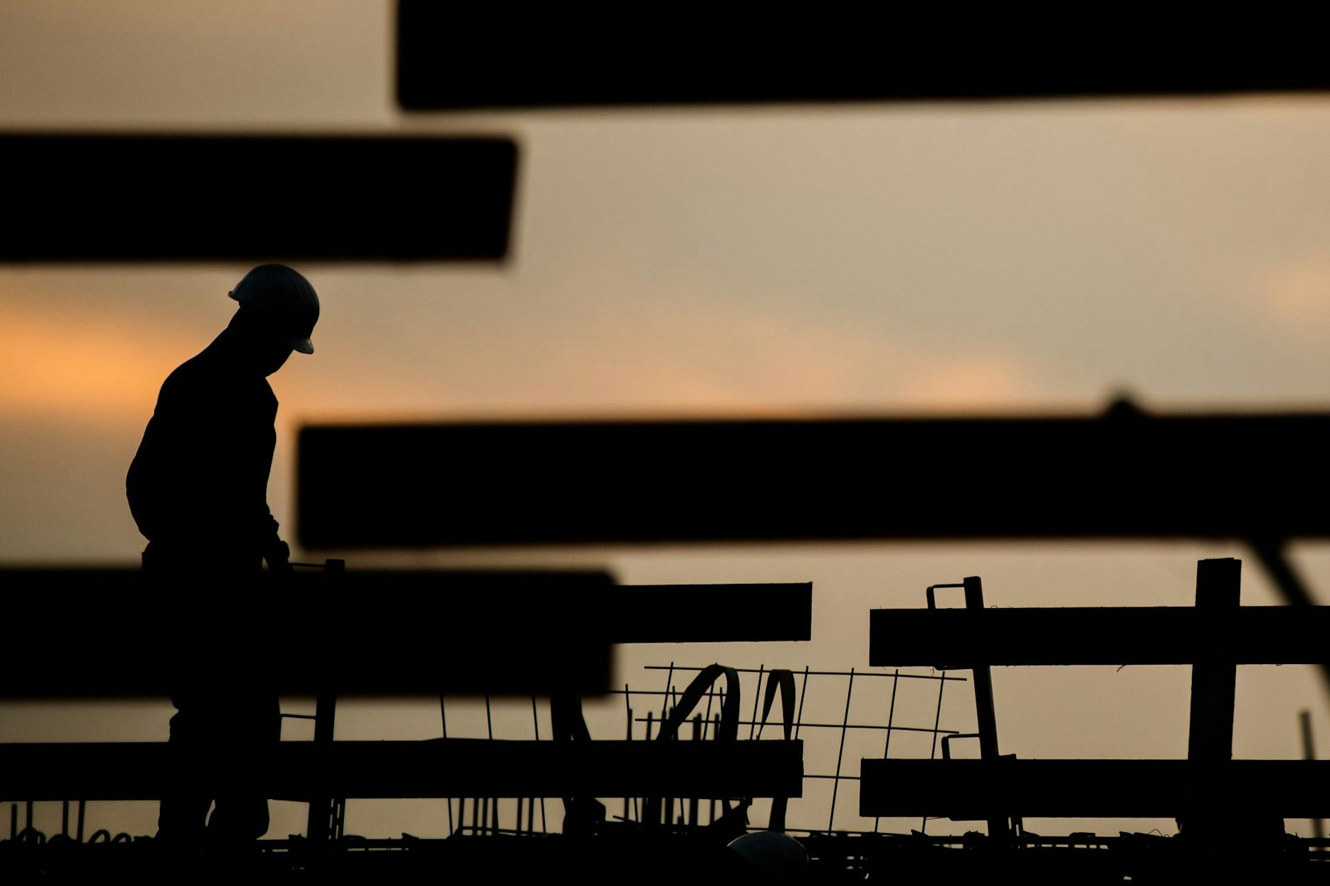 ARCHIV - Die Silhouette eines Bauarbeiters zeichnet sich auf einer Baustelle vor dem Morgenhimmel ab.