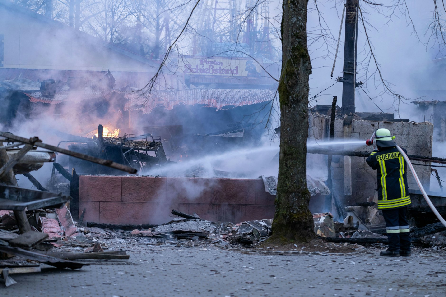 Feuerwehrmann strahlt Wasser auf verkohlte Gebäude- und Einrichtungsteile. Im Freizeit-Land Geiselwind ist ein Feuer ausgebrochen. Ein Kiosk und der Gaststättenbereich im Eingang des Freizeitparks sind vollständig zerstört. Die Löscharbeiten dauern an.