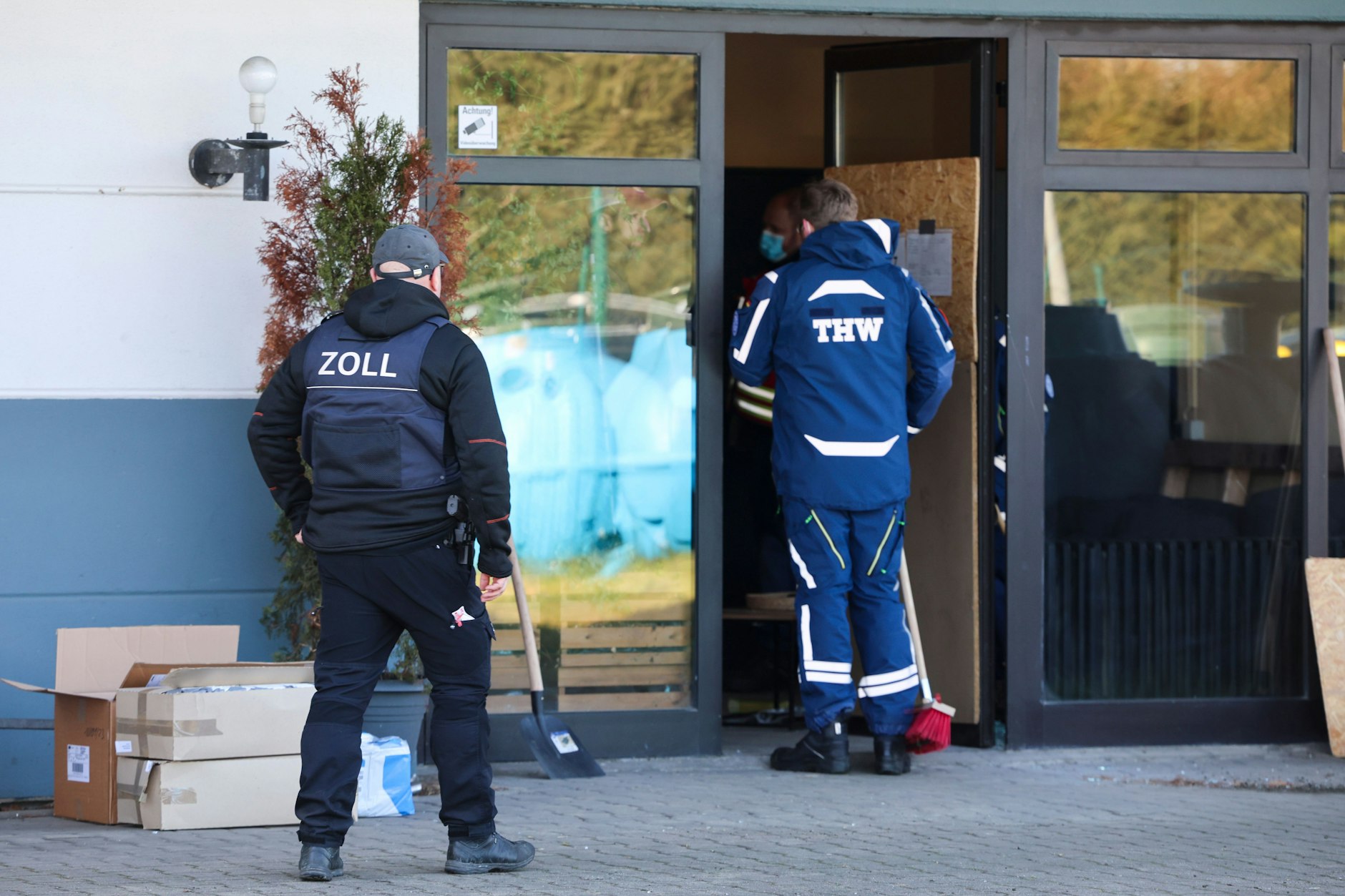 Düsseldorf: Ein Zollbeamter und mehrere Mitarbeiter des Technischen Hilfswerks stehen vor der Lagerhalle, in der der Zoll eine illegale Zigarettenfabrik durchsucht hat.