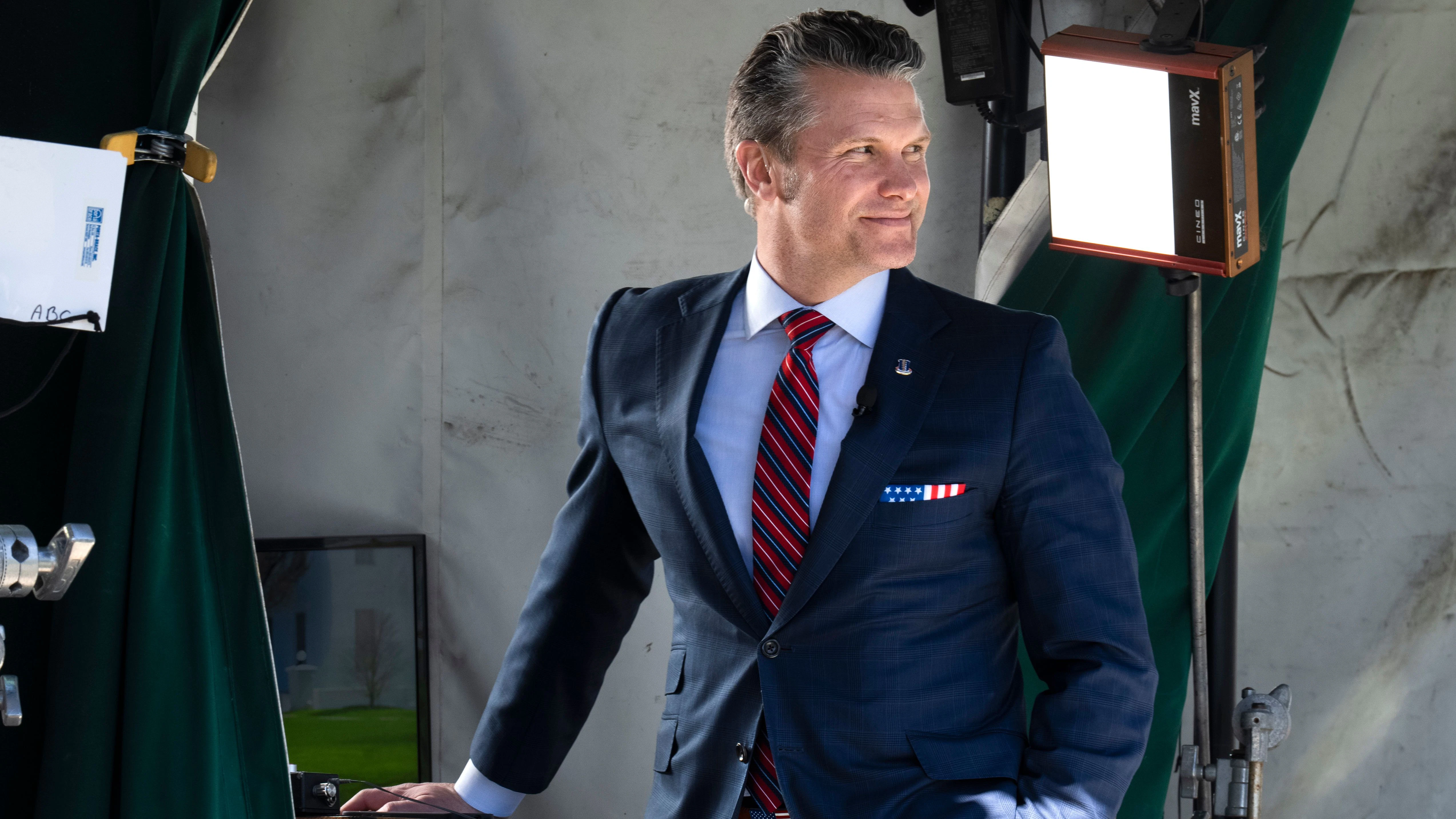 Wearing a U.S. flag themed pocket square and belt buckle, Defense Secretary Pete Hegseth waits for the start of a television interview outside the White House, Friday, March 21, 2025, in Washington. (AP Photo/Jacquelyn Martin)