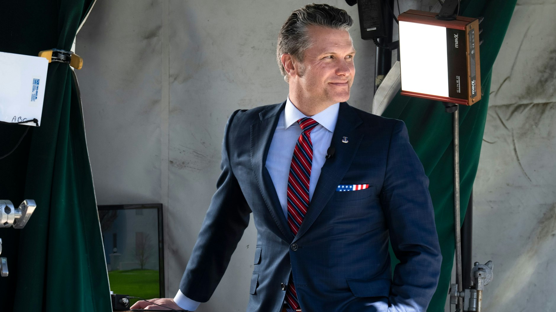 Wearing a U.S. flag themed pocket square and belt buckle, Defense Secretary Pete Hegseth waits for the start of a television interview outside the White House, Friday, March 21, 2025, in Washington. (AP Photo/Jacquelyn Martin)