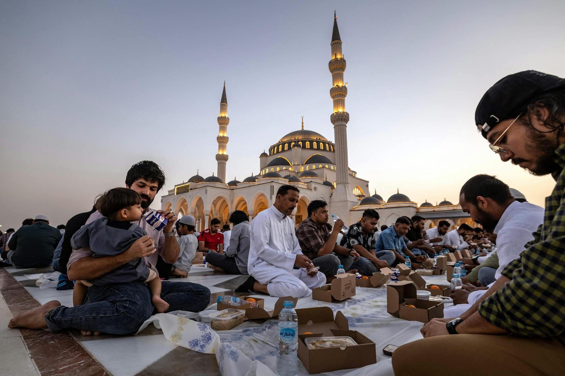 Gläubige beim abendlichen Fastenbrechen während des Ramadan vor einer Moschee im Emirat von Sharjah, VAE.