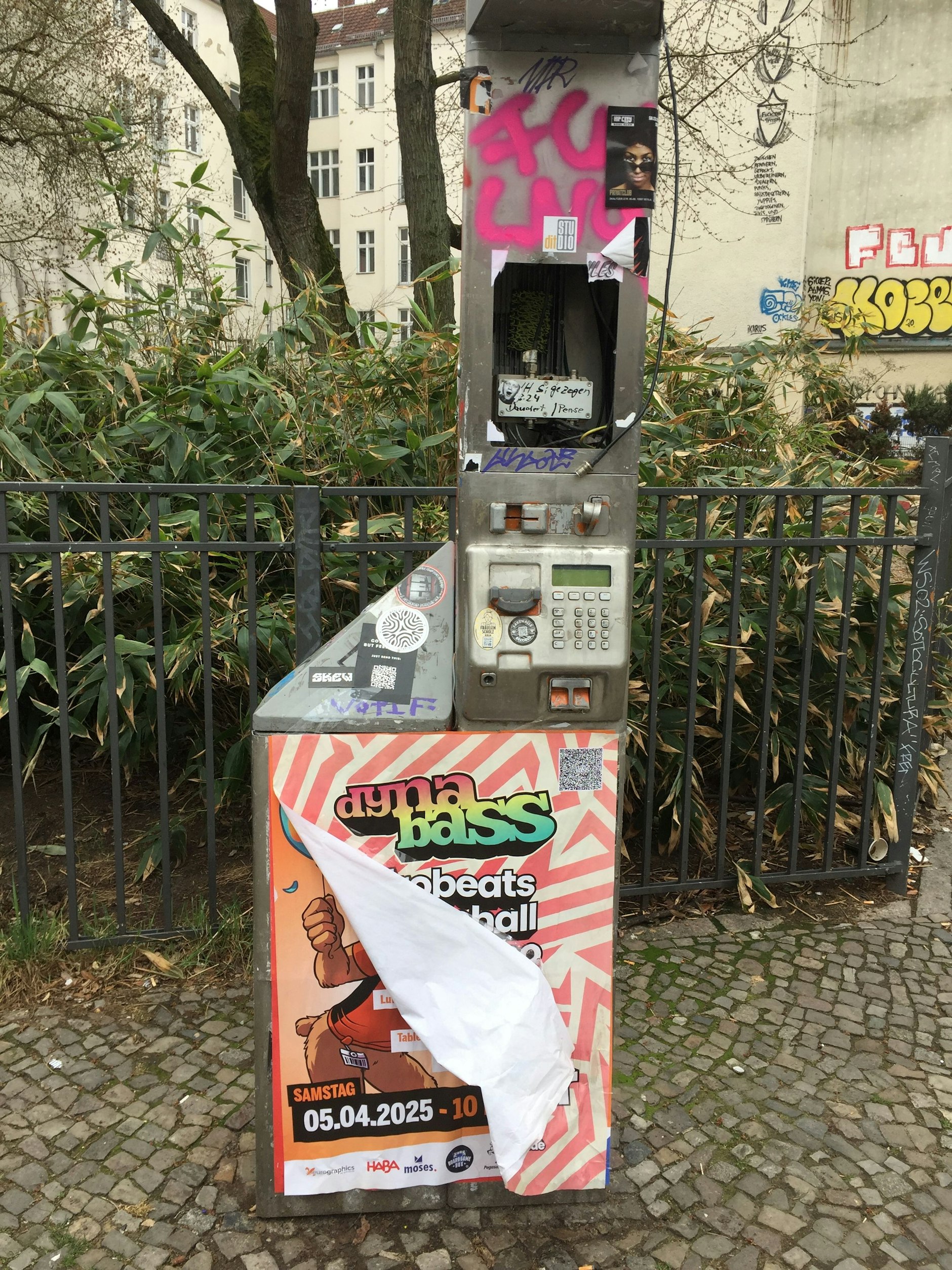 Typisches Berlin-Bild. Ein demoliertes öffentliches Telefon ist mit Plakaten vollgehängt.