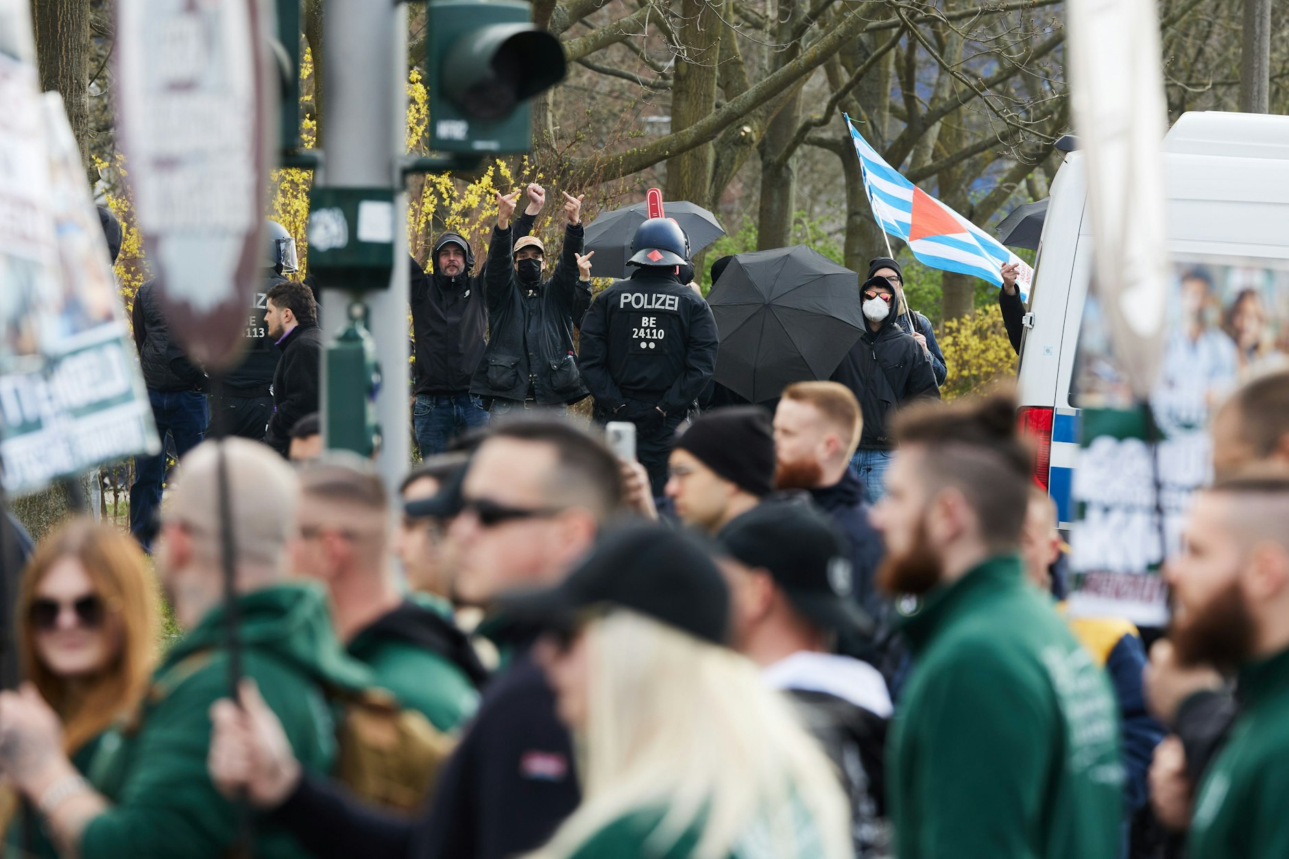 Teilnehmer einer Demonstration der rechtsextremistischen Kleinstpartei III. Weg marschieren durch Hellersdorf, während im Hintergrund Gegenproteste stattfinden. 