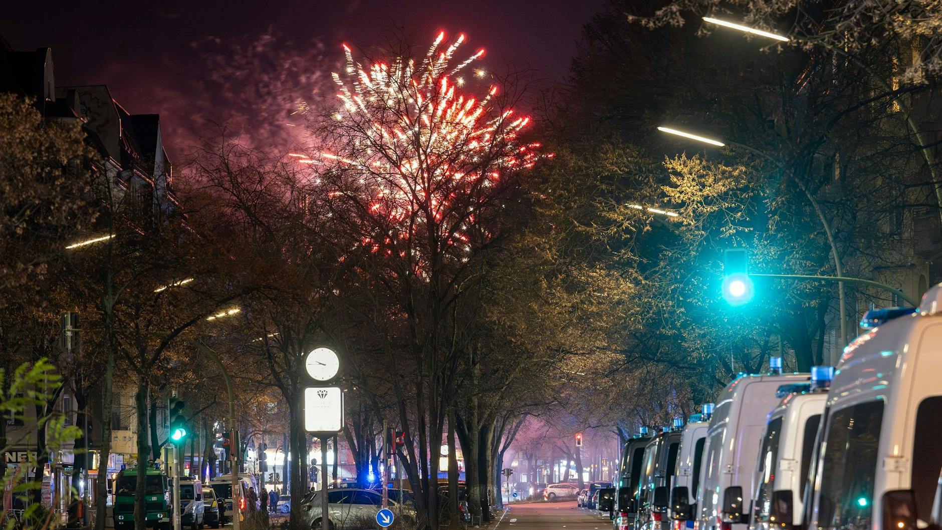 In der Silvesternacht 2024/25: Fahrzeuge der Polizei stehen in der Sonnenallee im Stadtbezirk Neukölln in der Verbotszone für Feuerwerk. Im Hintergrund außerhalb der Zone ist am Himmel Feuerwerk zu sehen.