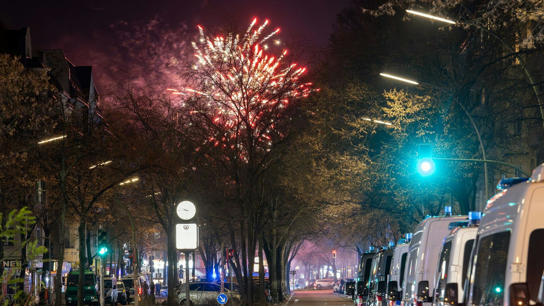 In der Silvesternacht 2024/25: Fahrzeuge der Polizei stehen in der Sonnenallee im Stadtbezirk Neukölln in der Verbotszone für Feuerwerk. Im Hintergrund außerhalb der Zone ist am Himmel Feuerwerk zu sehen.