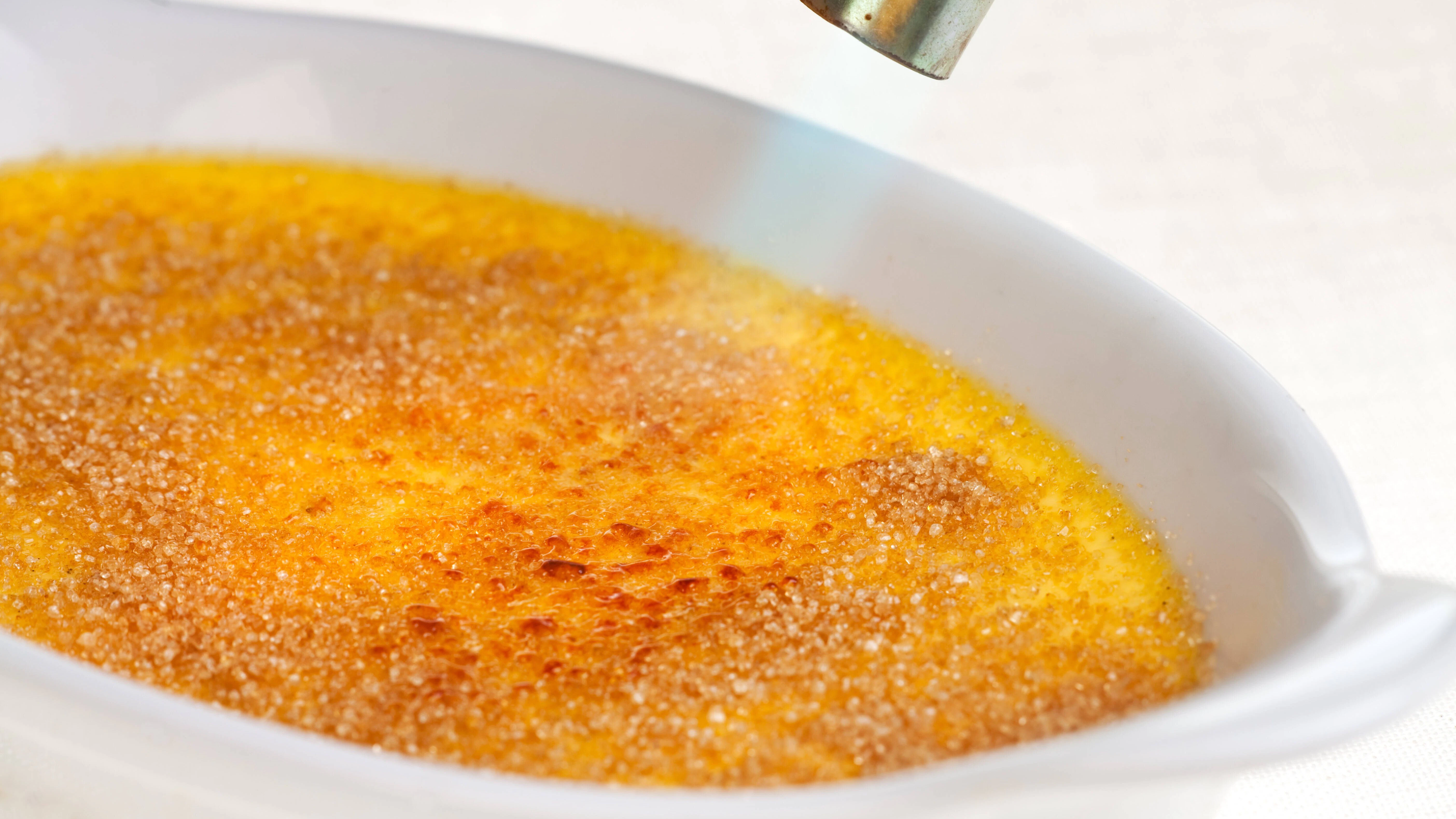 Crème brûlée karamellisieren: Auf die fertige Sahne-Creme&nbsp; wird Zucker gestreut, der dann mit dem Brenner geflammt wird.