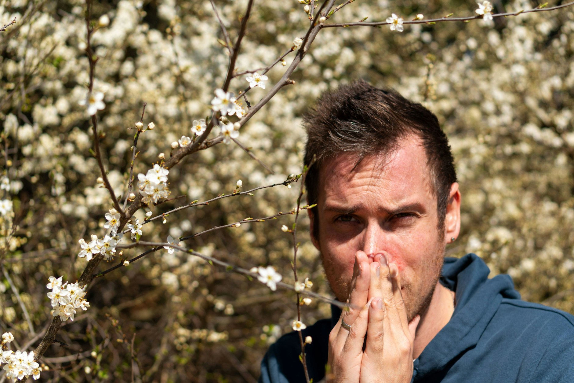 Ein Mann kämpft gegen die typischen Heuschnupfen-Symptome: tränende Augen und verstopfte Nase.